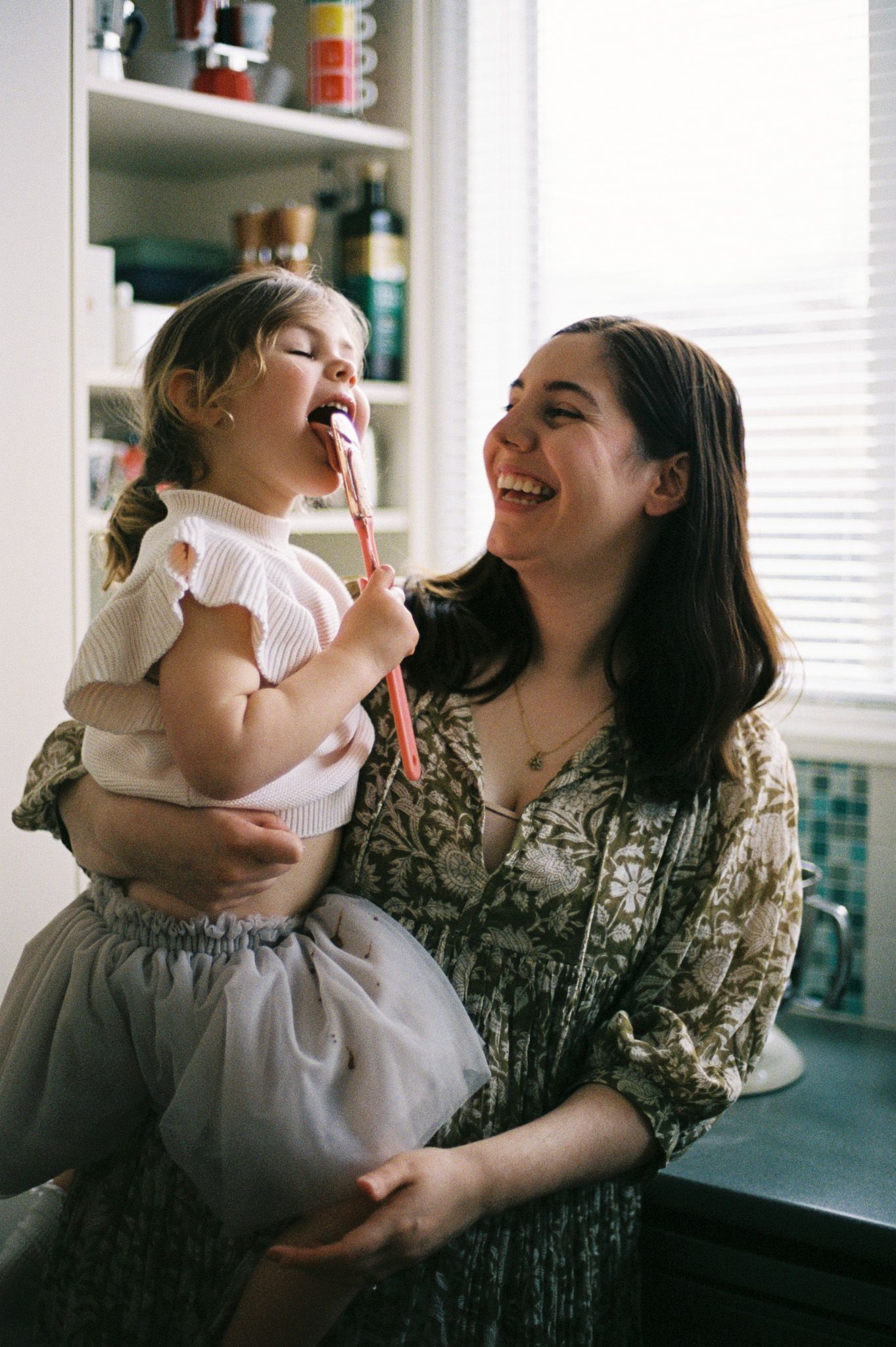 Joyful indoor scenes showing playful interactions and laughter in a bright kitchen setting during a Melbourne motherhood session.