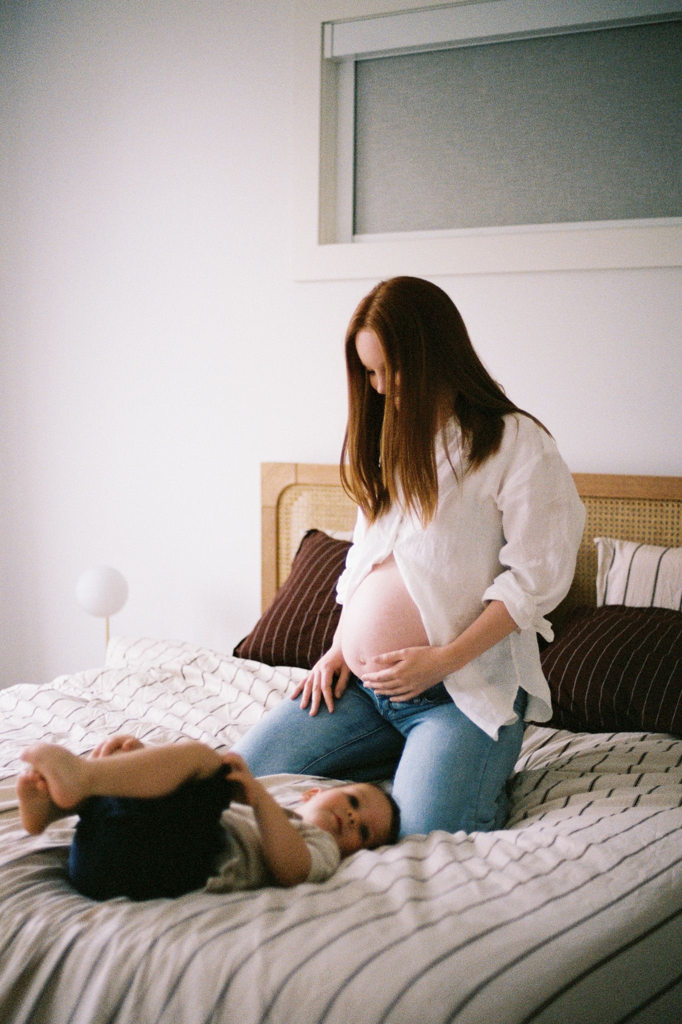 Two people in casual clothing share an intimate moment while sitting together on a bed with white linens.