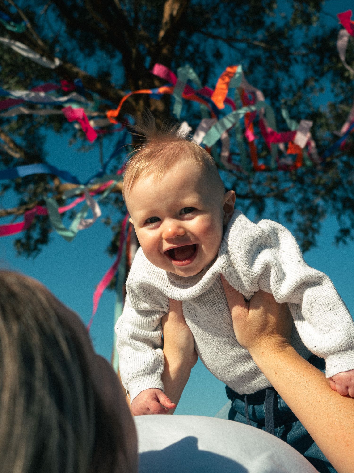 Happy baby against blue sky with colorful decorations overhead.