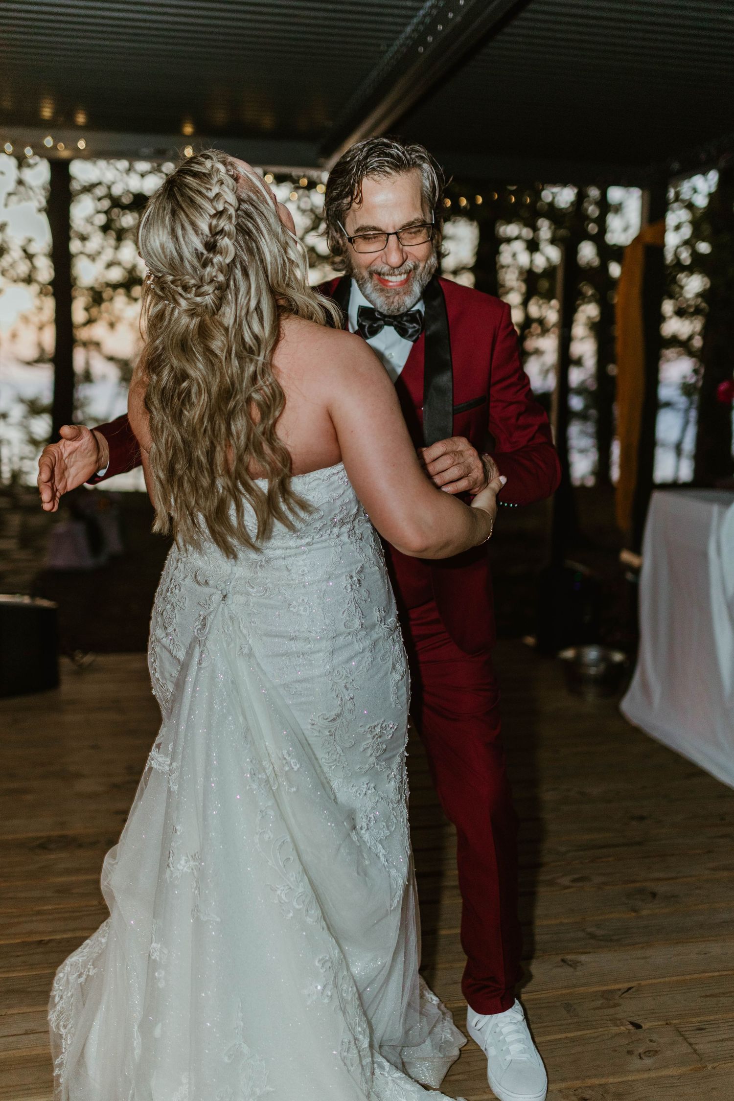 Wedding couple dancing together on wooden floor with one wearing burgundy suit and other in white dress.