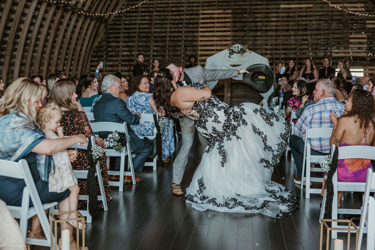 Wedding reception scene in a rustic barn venue with guests seated at long tables.
