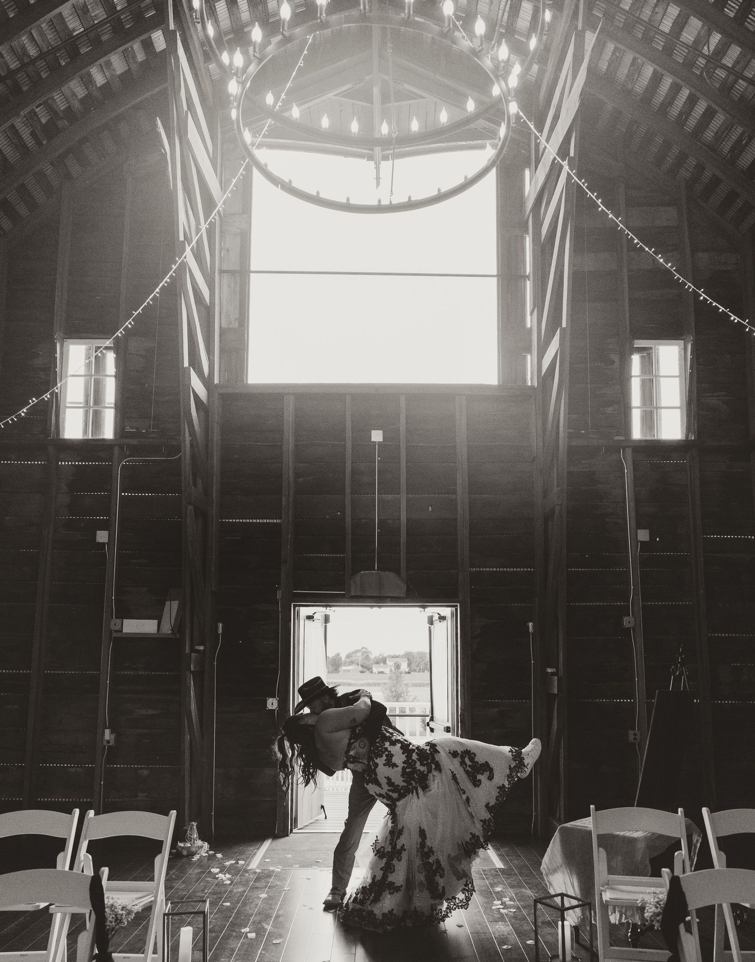 Rustic barn wedding venue interior with string lights and dramatic window lighting.