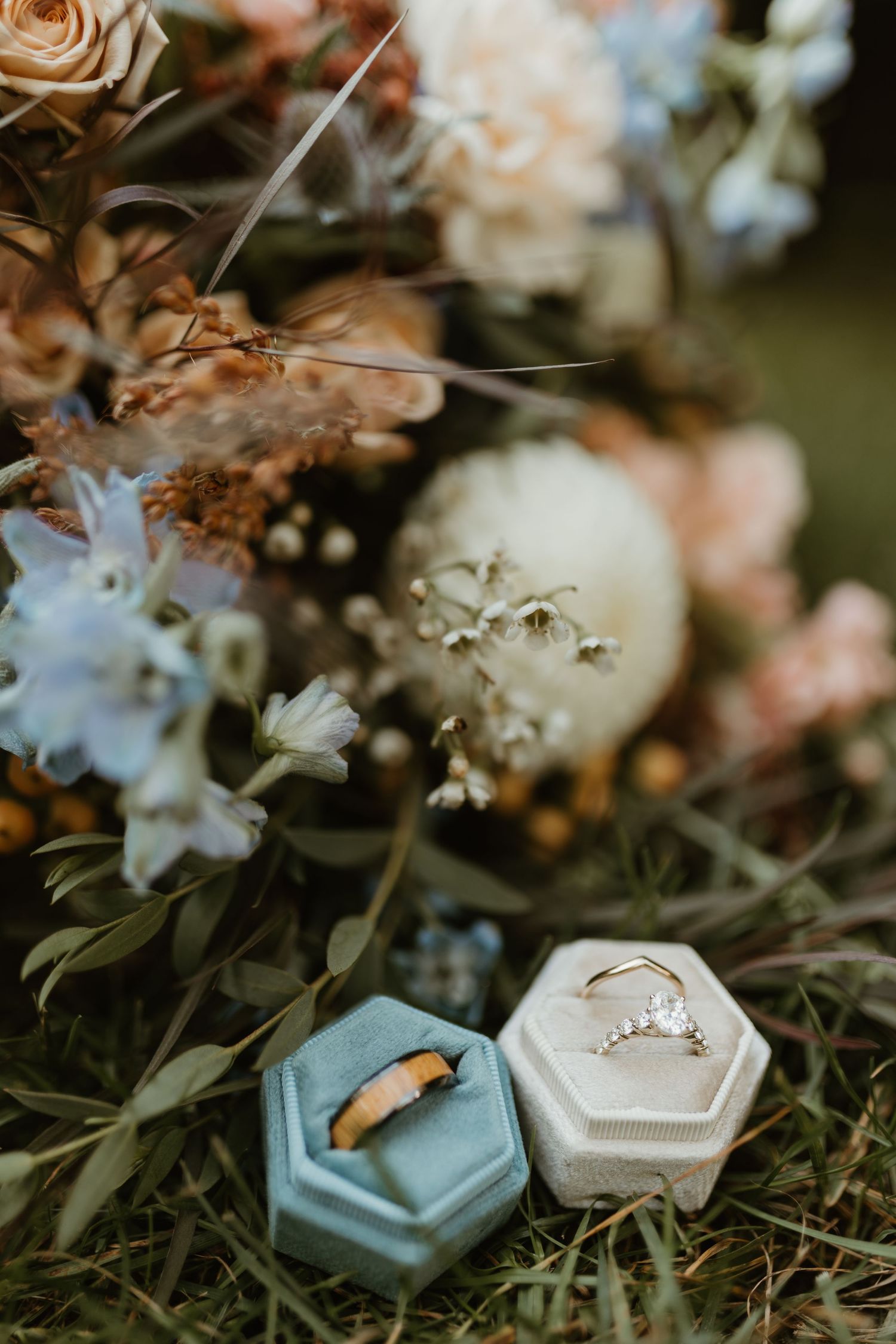 Wedding rings and jewelry displayed in pale blue and white velvet ring boxes among delicate flowers.