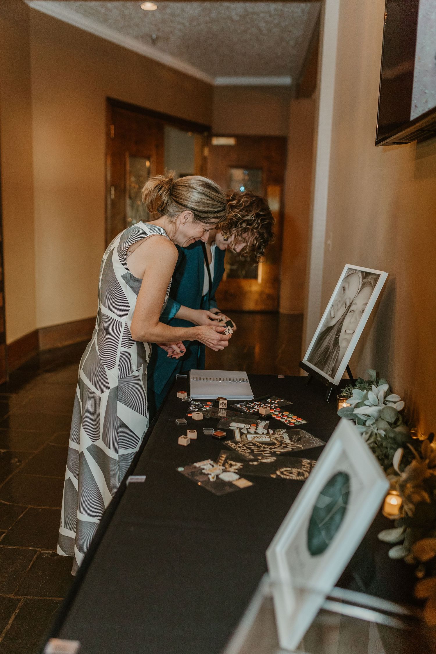 Two guests look at photos displayed on a memorial table at a wedding reception.