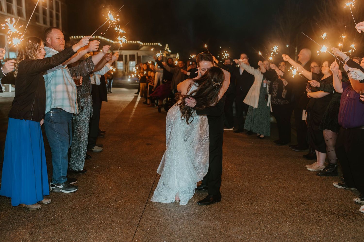 Wedding guests hold sparklers creating a magical nighttime exit tunnel for the newlyweds.