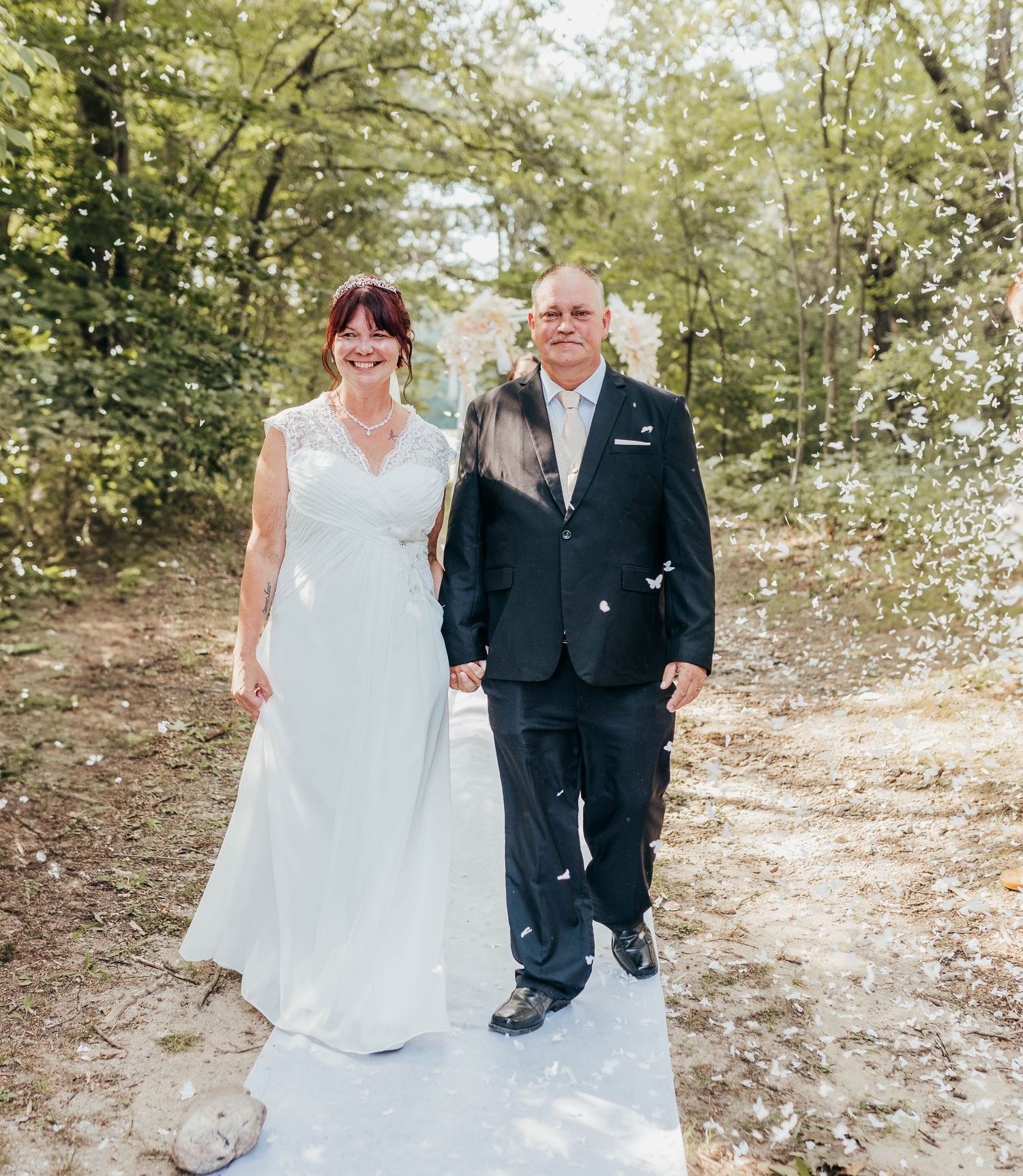 A couple walking along a sunlit forest path during their wedding celebration.