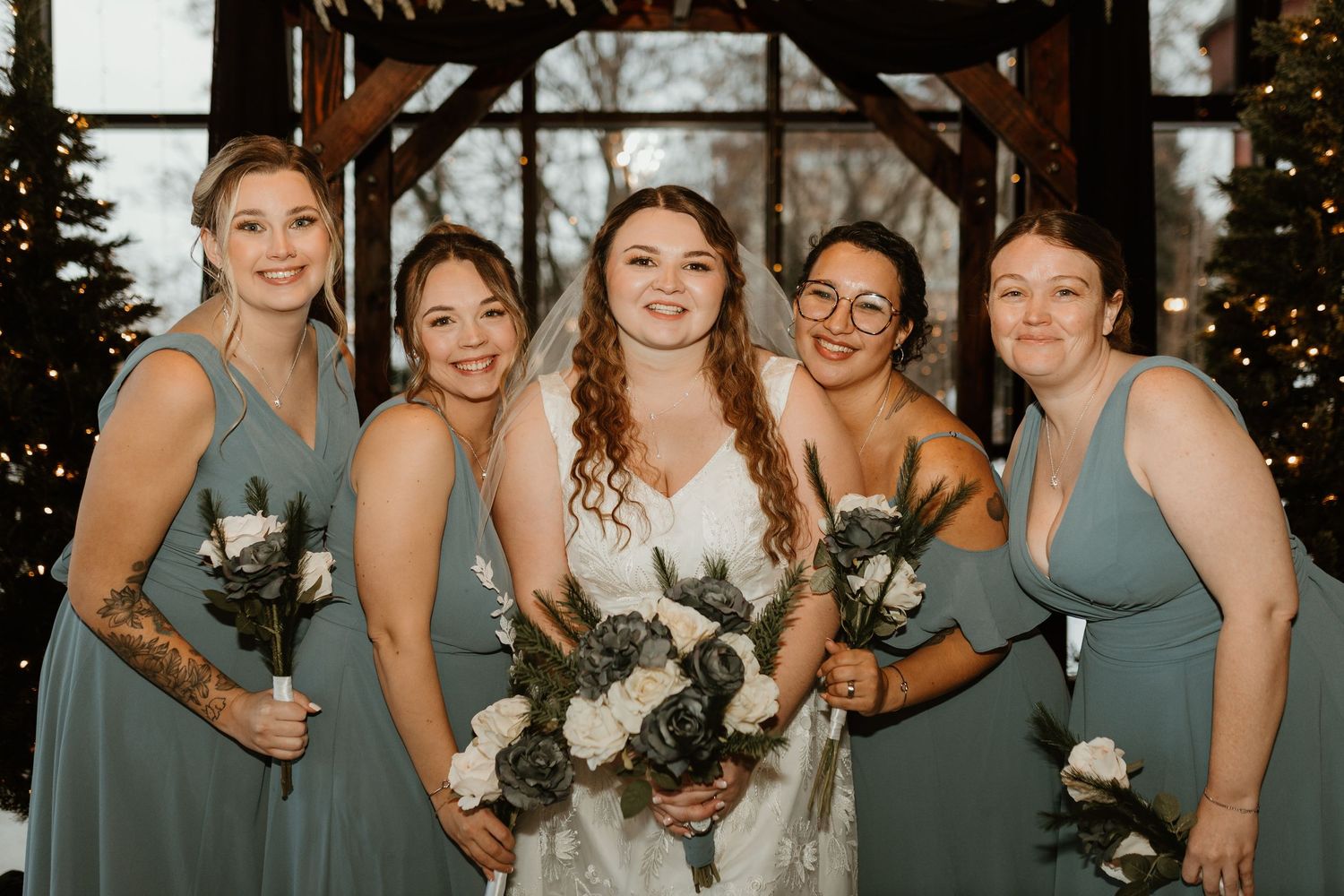 Bridesmaids in sage green dresses pose together at an indoor wedding venue.