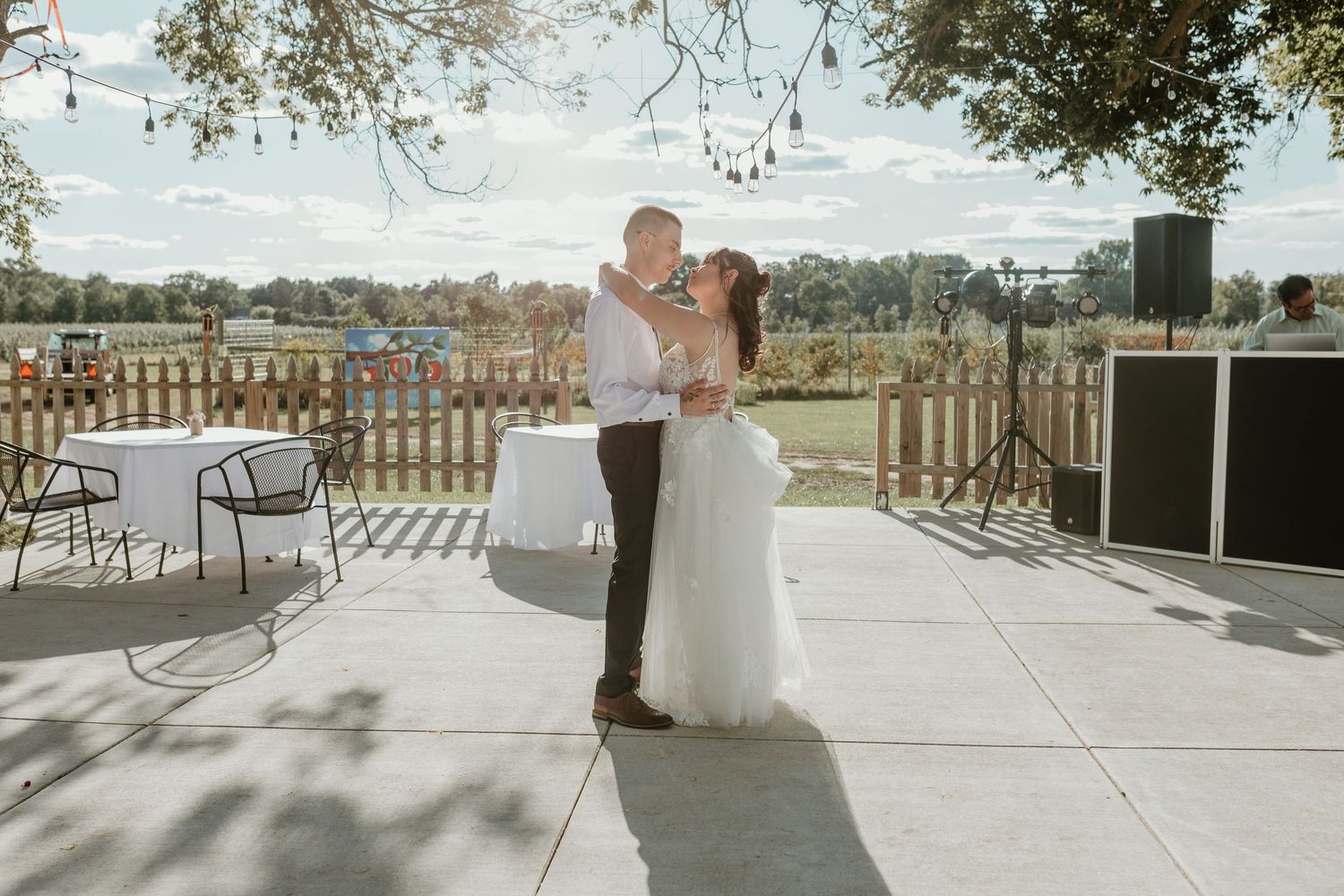 A wedding couple shares a romantic moment on a sunlit stone patio with scenic views.