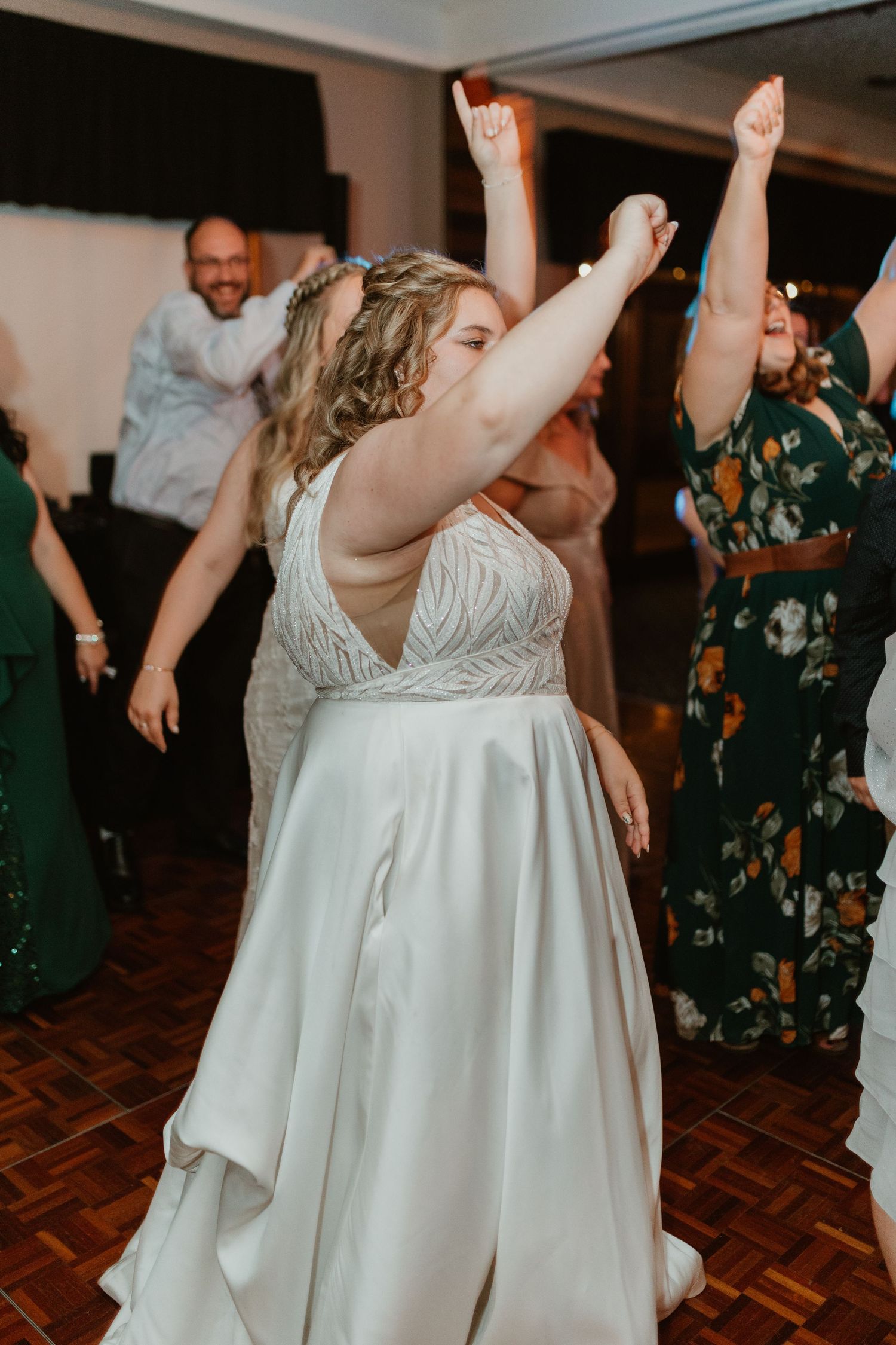 A bride in a white dress dances joyfully with raised arms at the wedding reception.