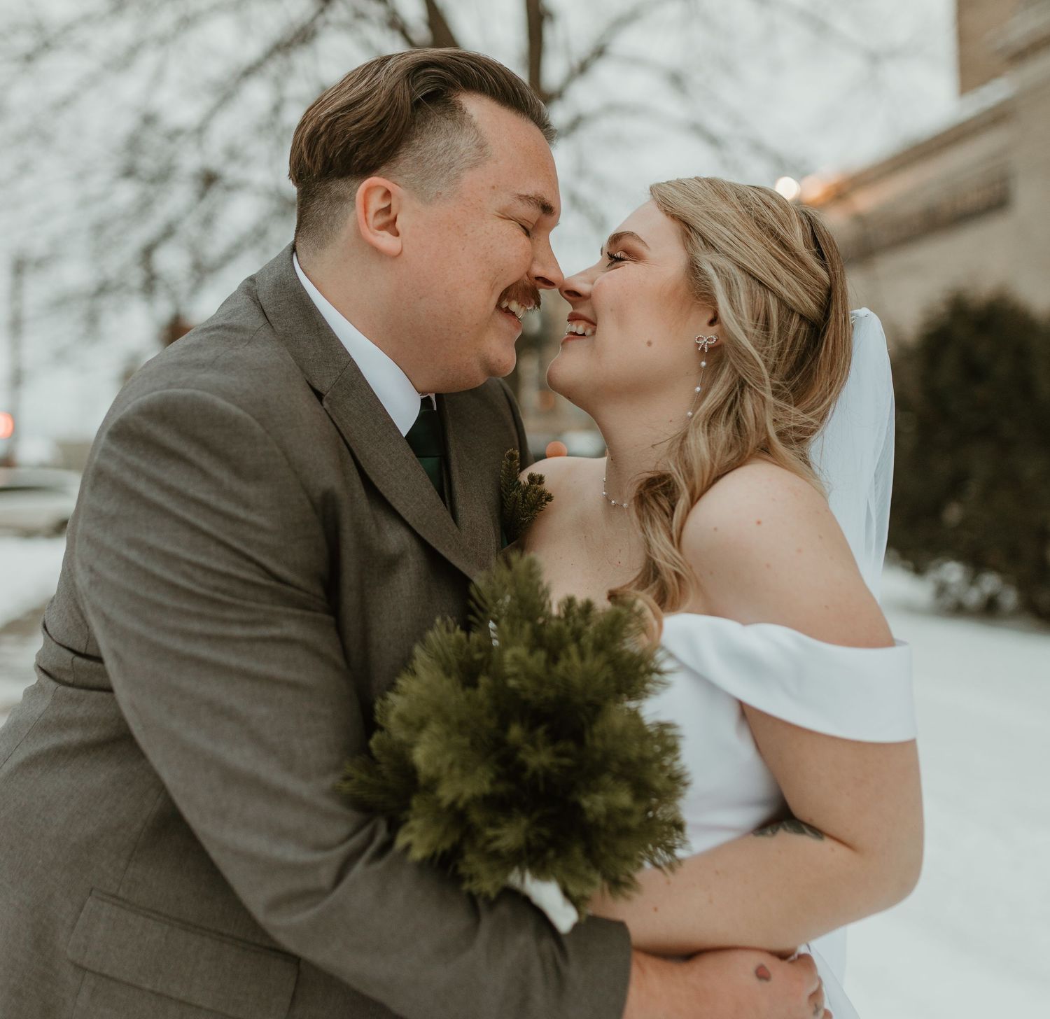 Winter wedding portraits with evergreen bouquet against snowy backdrop.