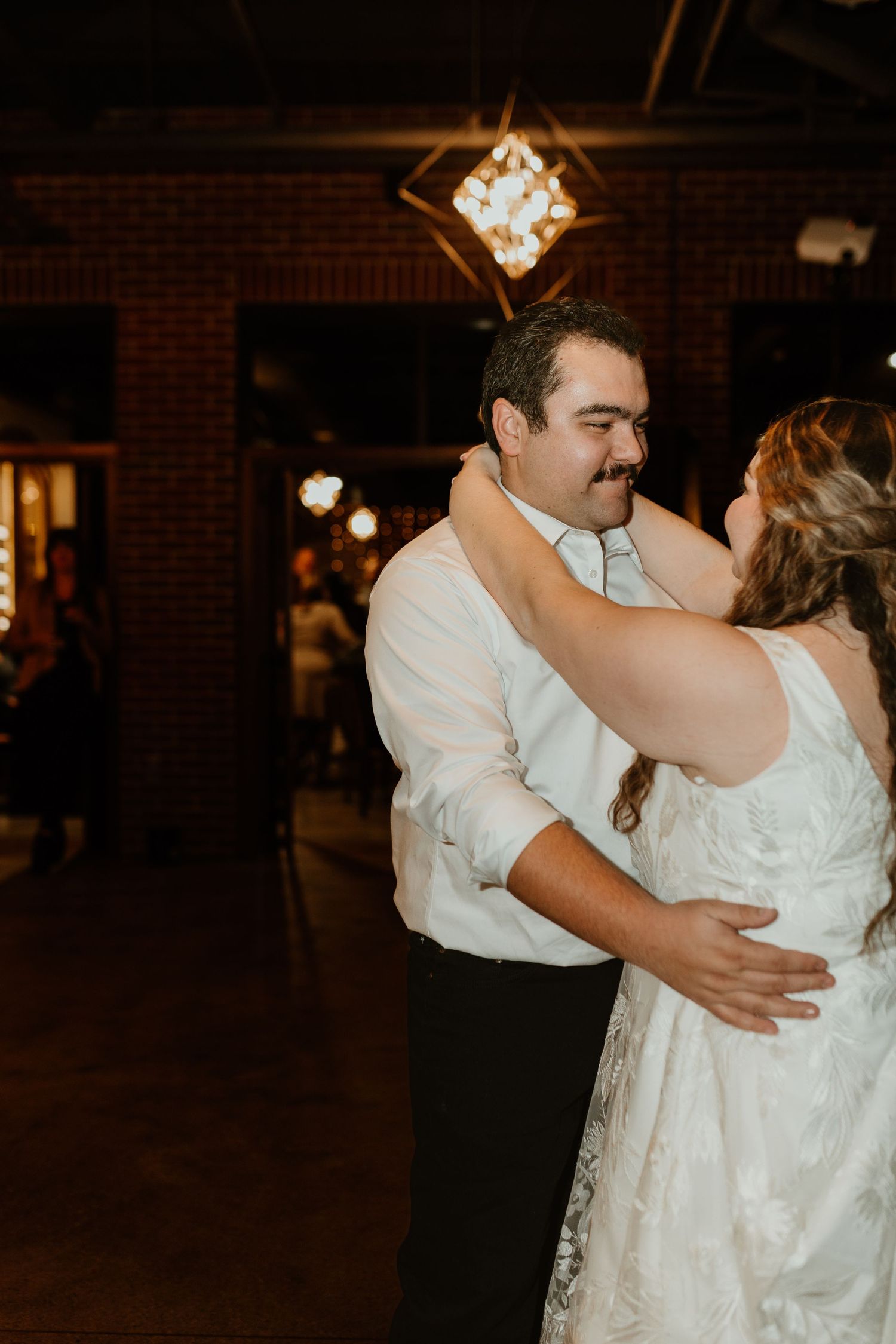 Tender first dance moment between newlyweds in dimly lit reception venue.