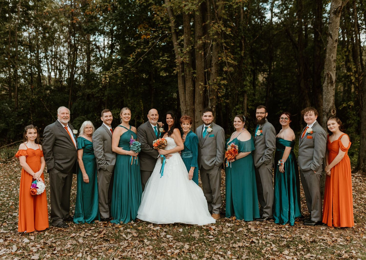 Wedding party in teal and orange dresses poses together in an autumn setting.