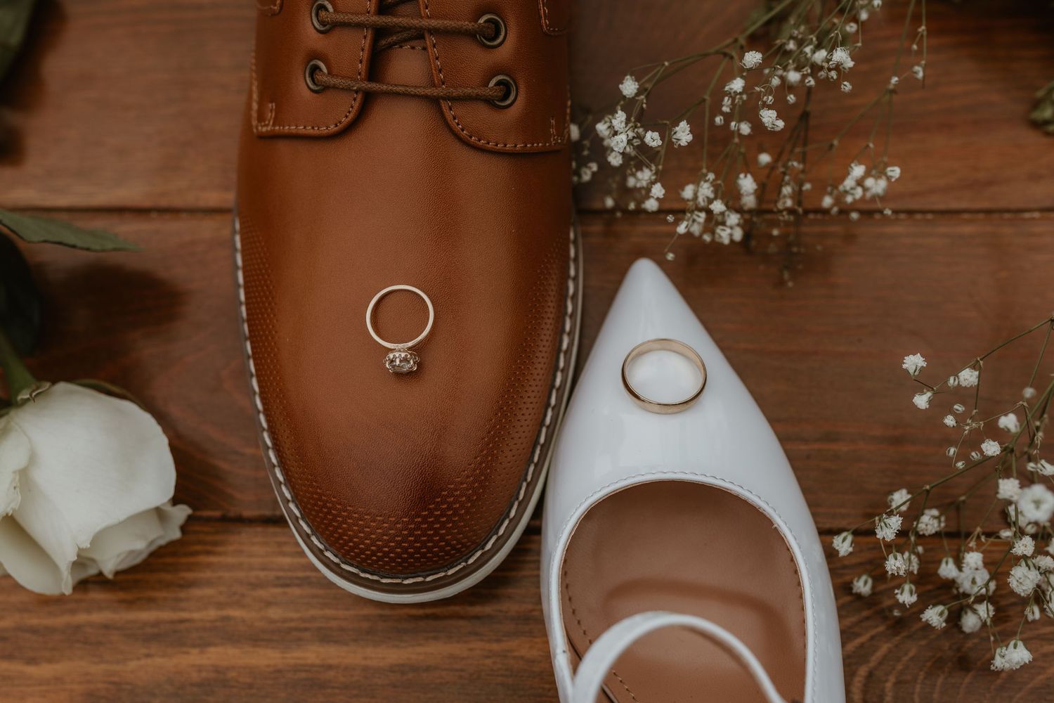 Wedding accessories including rings, shoes, and baby's breath flowers arranged on a wooden surface.