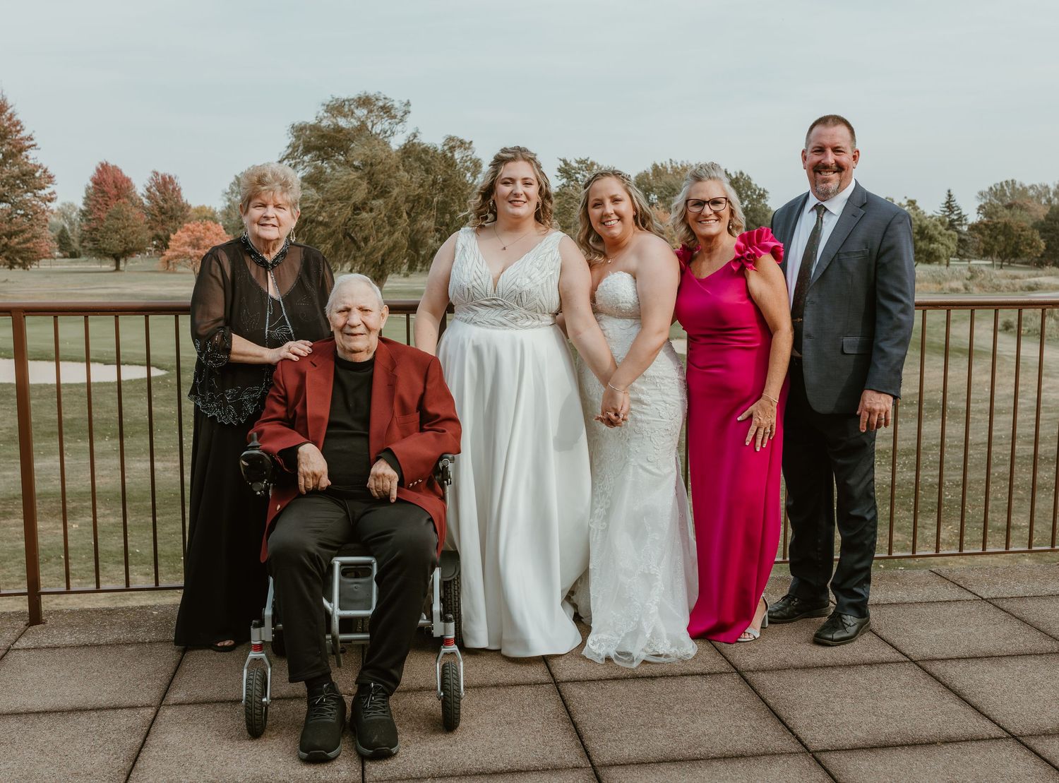 Wedding group photo with family and friends in mix of formal attire on outdoor patio.