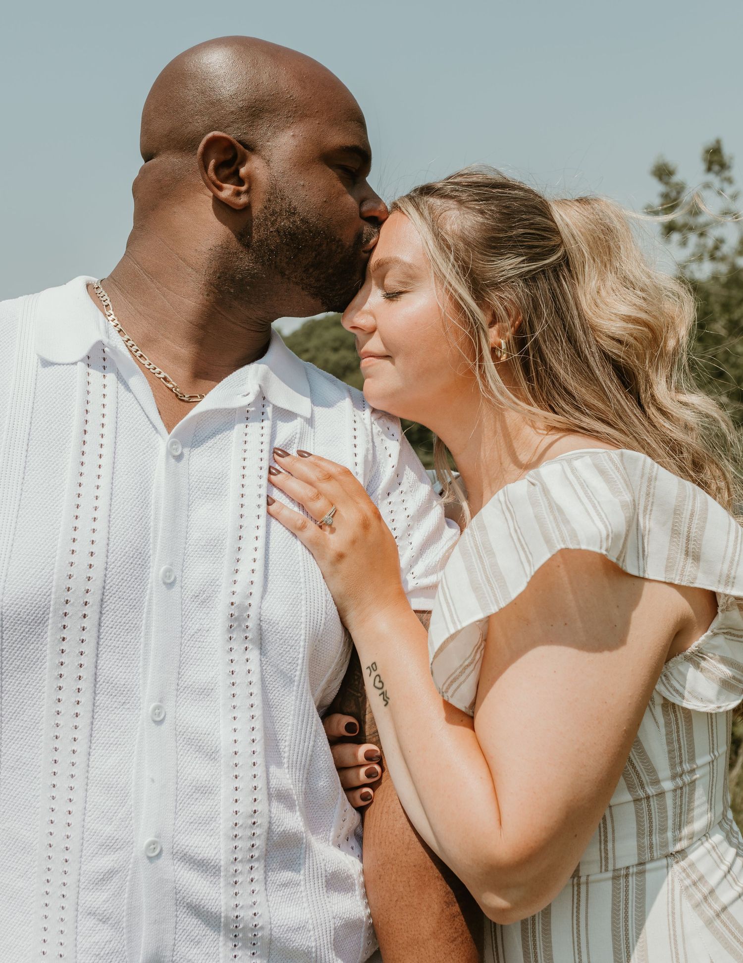 A couple in white wedding attire shares intimate moments during an outdoor photoshoot.