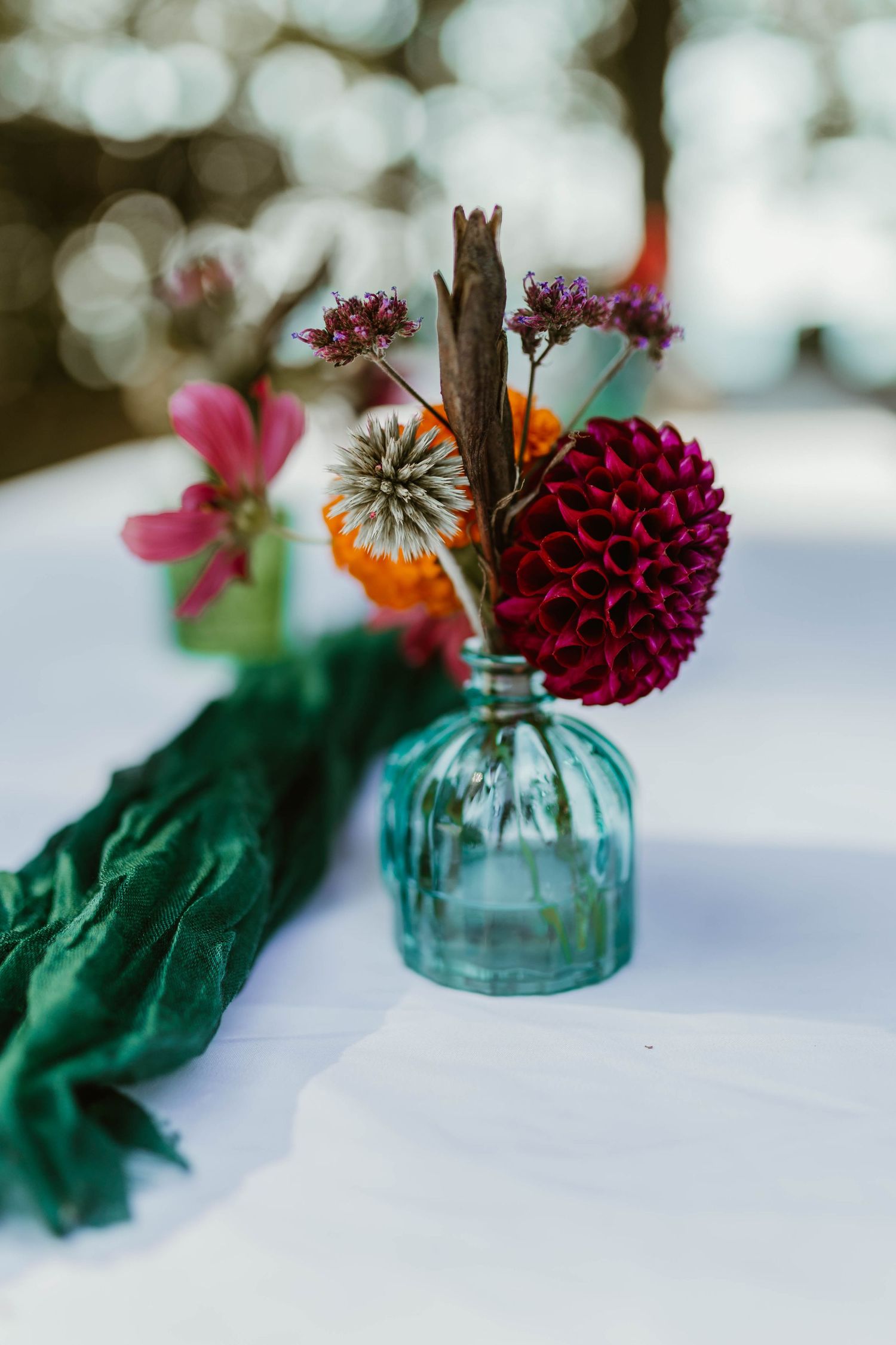 Colorful wedding centerpiece with burgundy dahlia flowers in blue vintage glass vases.