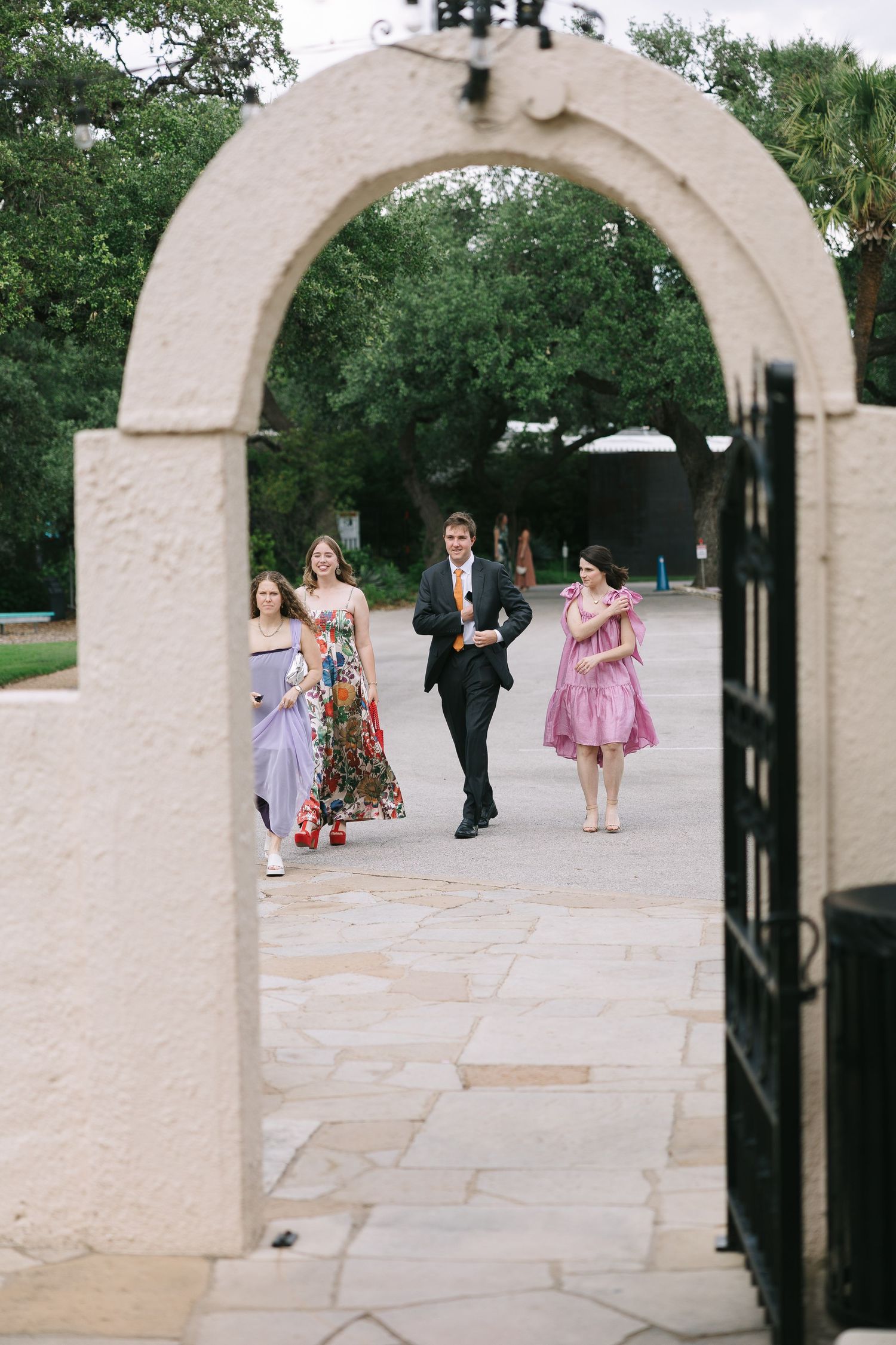 White stone archways frame guests walking along a garden pathway during an outdoor event.