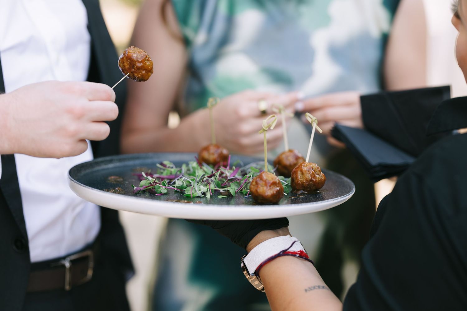 Hands holding plates of appetizers at an outdoor wedding reception.