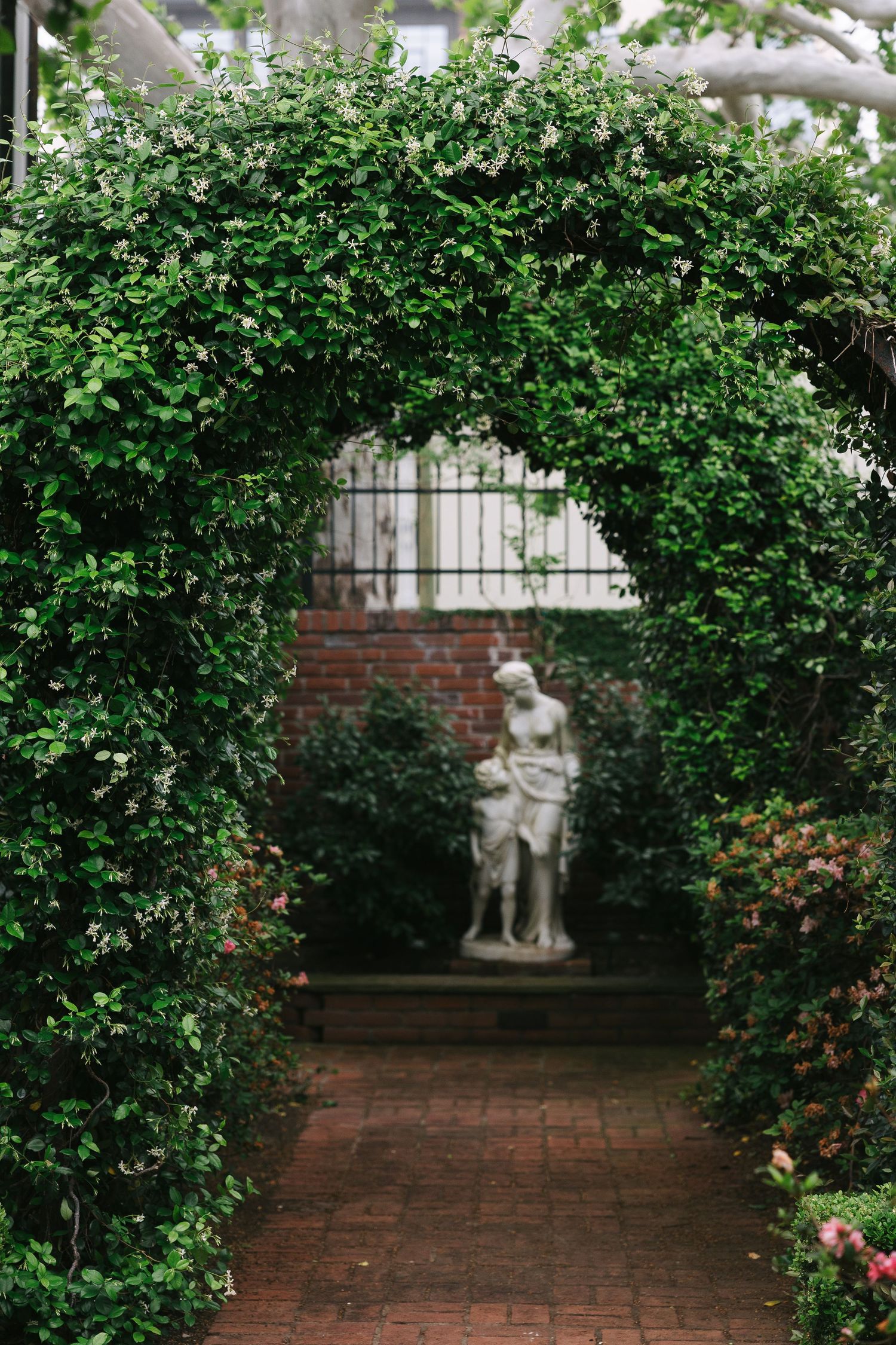 Garden courtyard with brick pathways and classical statues surrounded by lush green hedges.