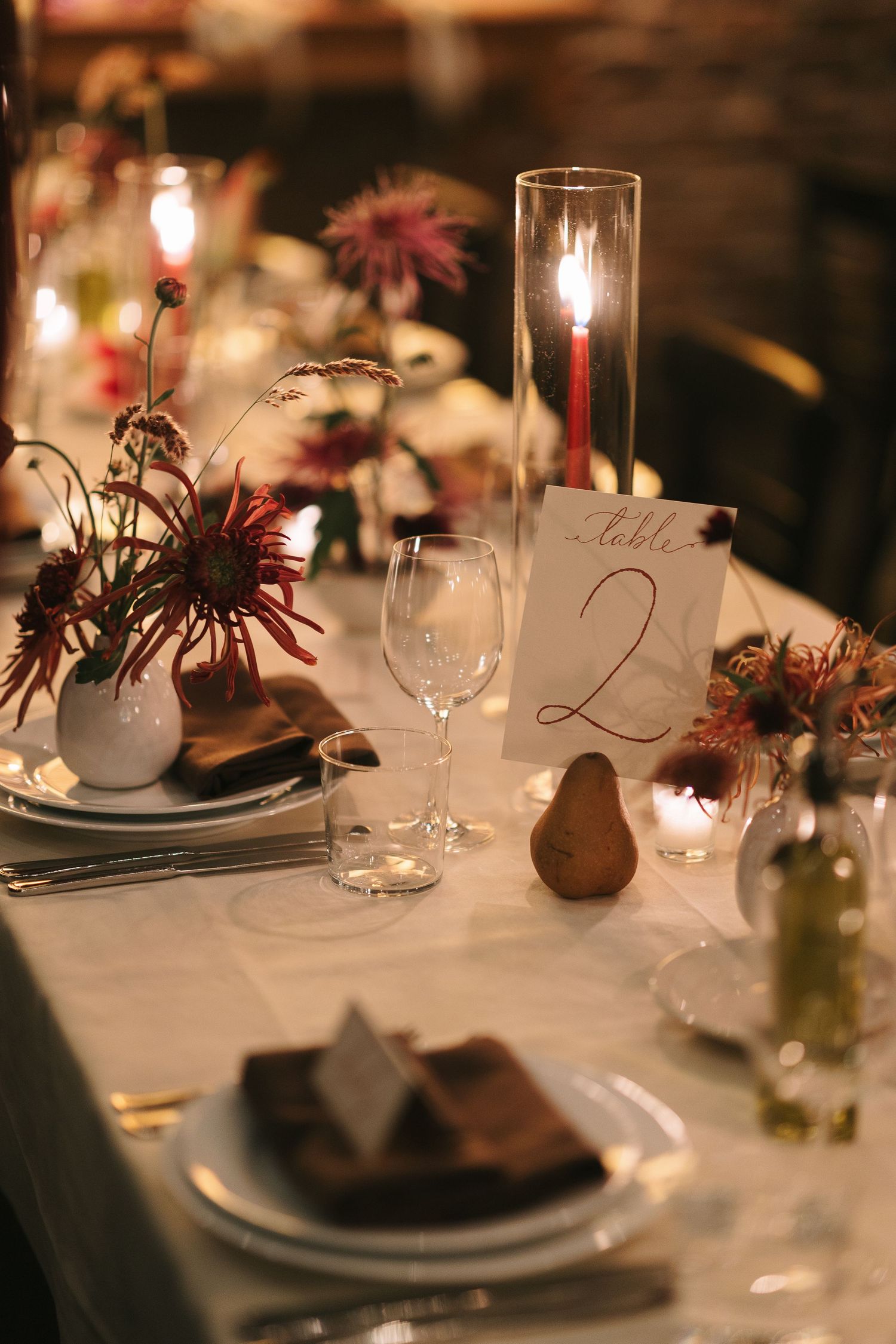 Romantic candlelit wedding reception table with burgundy floral accents and wine glasses.