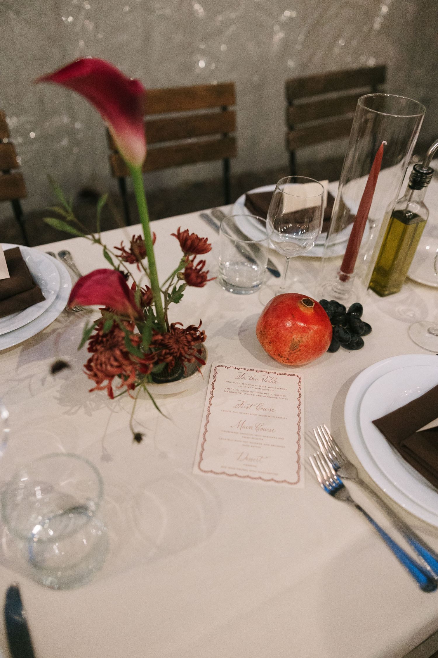 Table setting with red calla lily centerpiece, pomegranate, and menu card on white tablecloth.