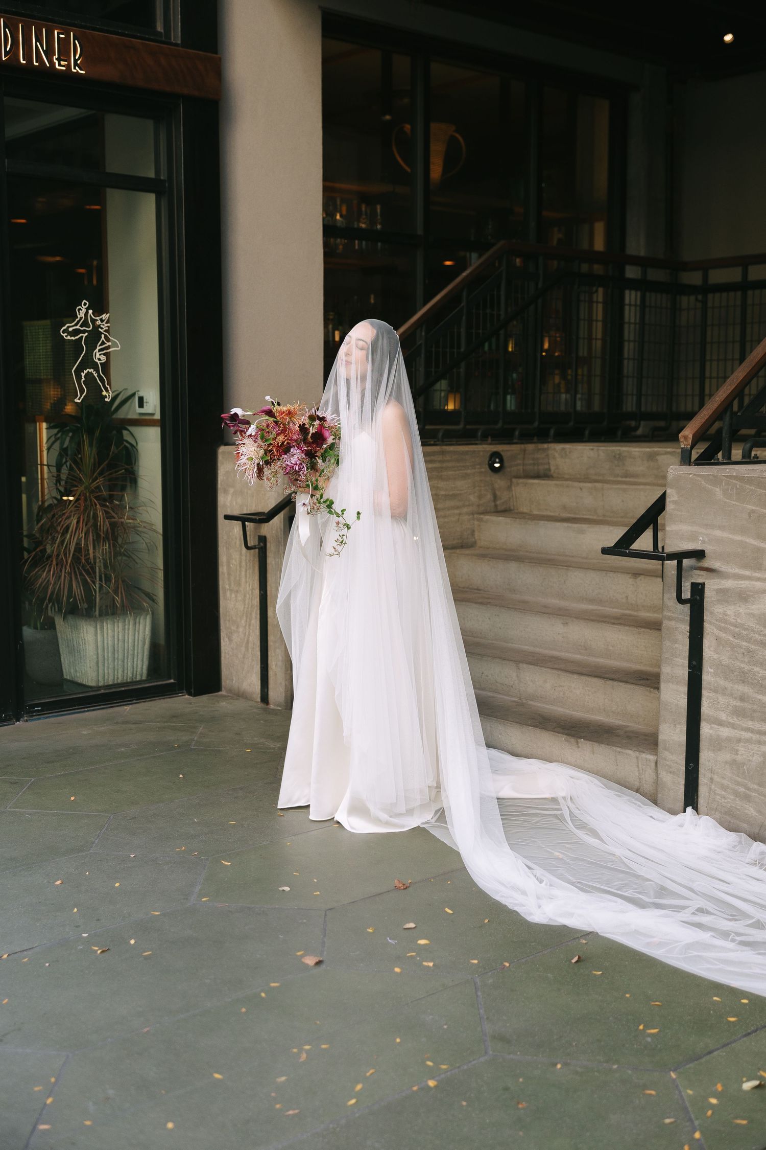A dramatic bridal portrait on concrete stairs with flowing white dress and trailing veil.