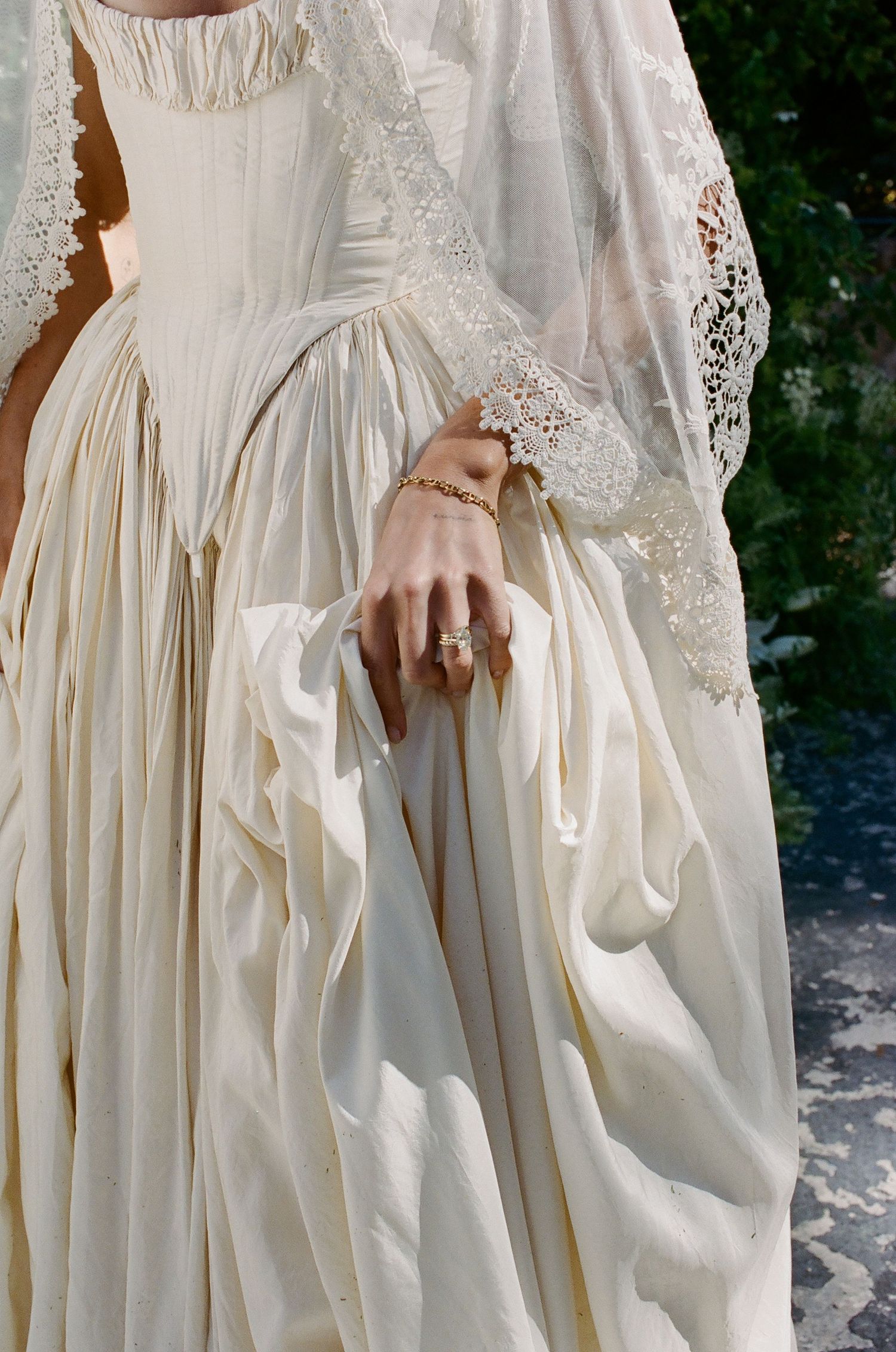 Close-up of a bride in an ivory gown with lace veil, wearing gold chain bracelet and diamond ring.