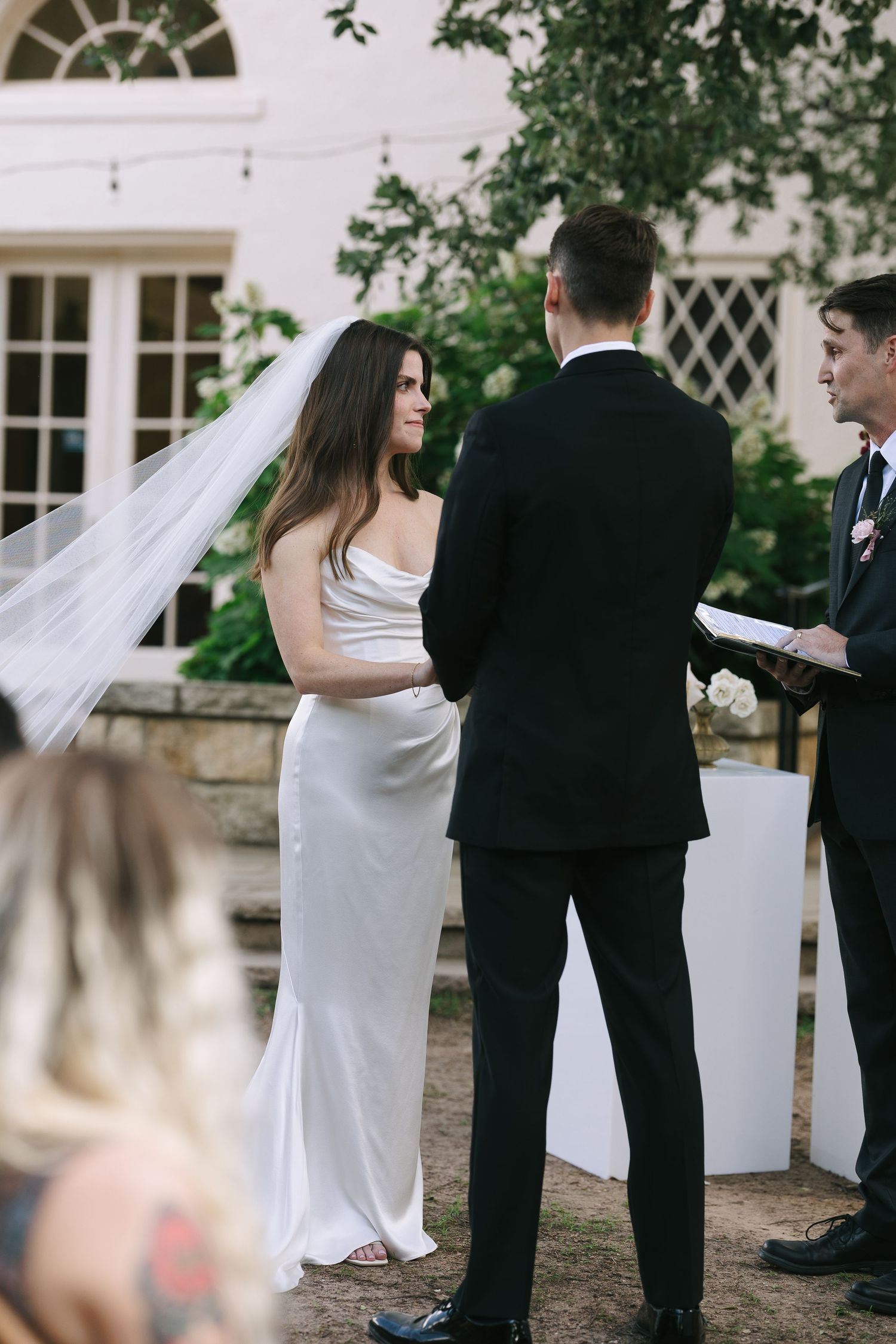 Elegant outdoor wedding ceremony with couple and officiant in front of white building.