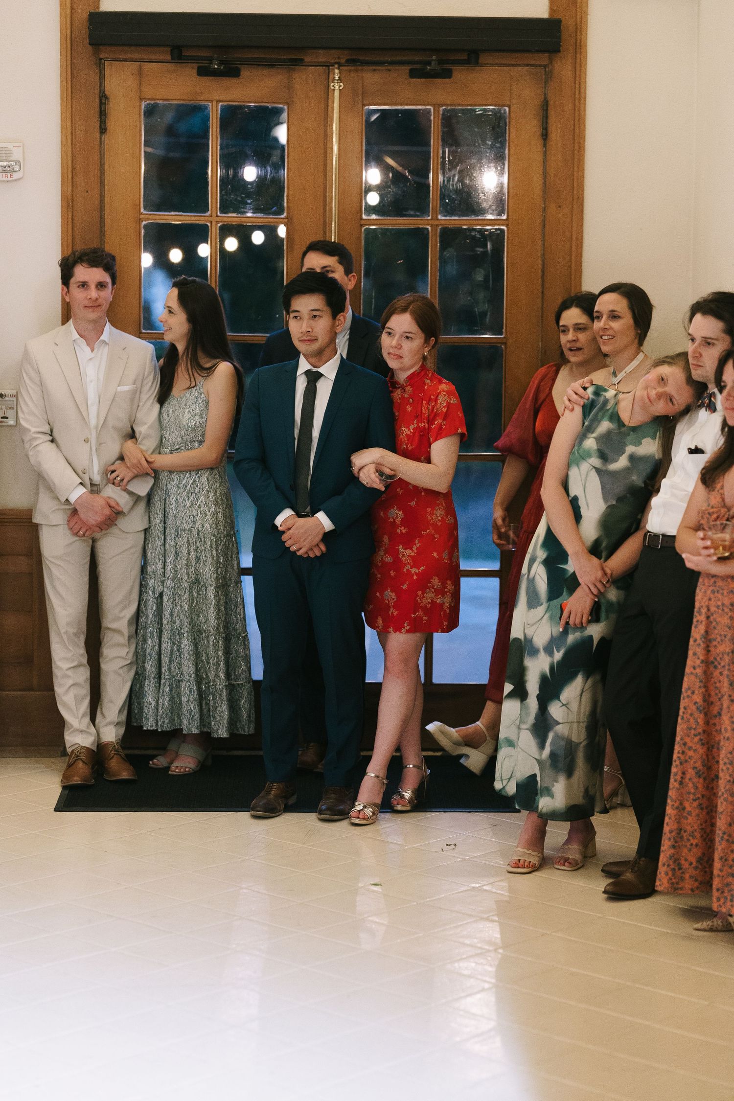 Wedding guests lined up against a wall at an indoor venue with wooden trim.
