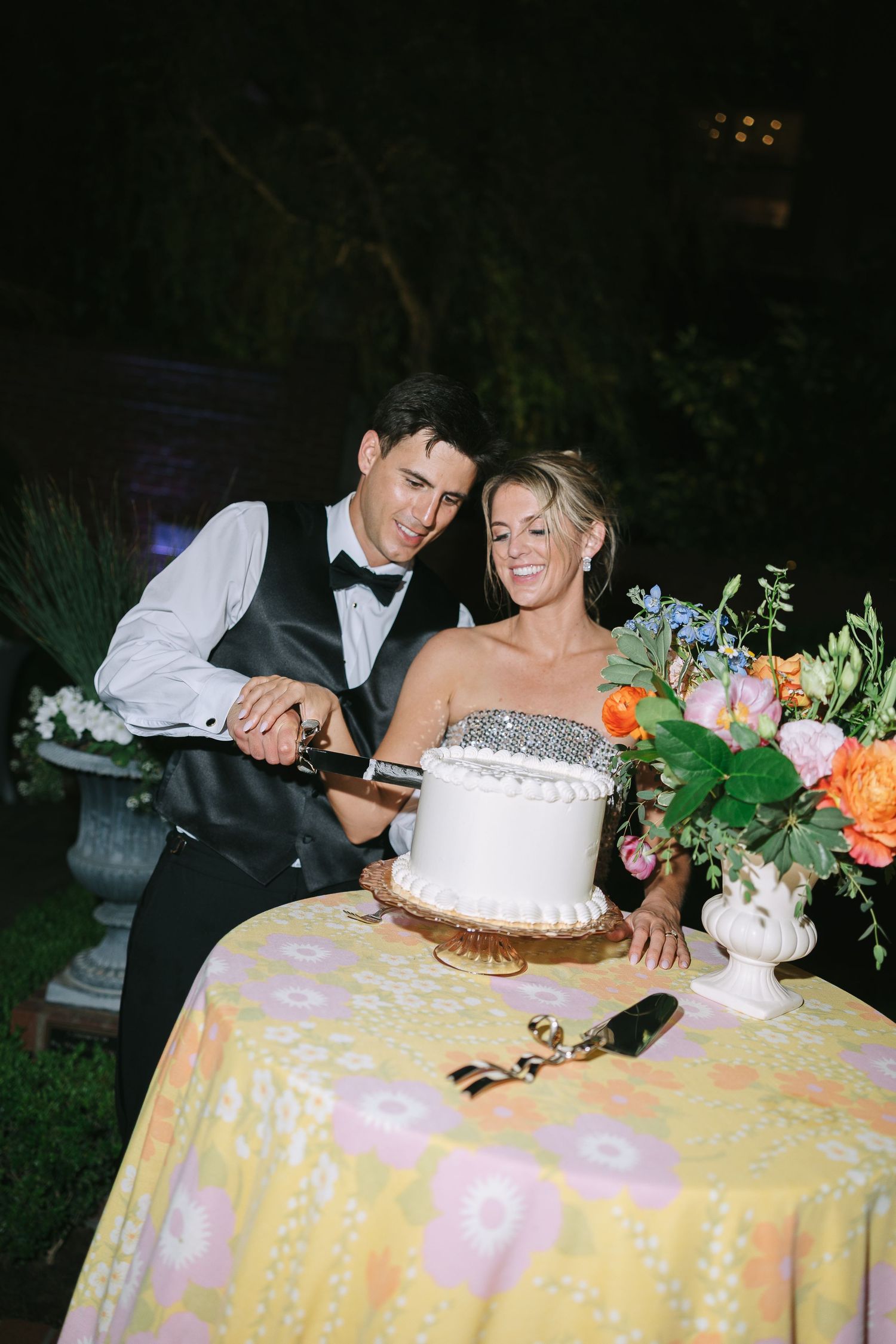 Newlyweds cutting their white wedding cake together on a decorated table.