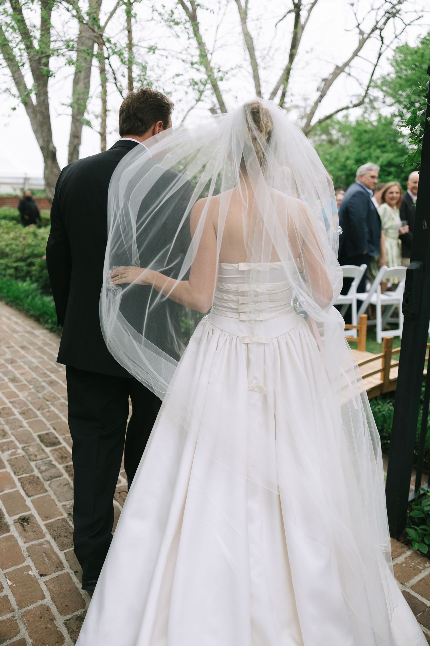 Back view of white wedding dress with veil during outdoor ceremony.