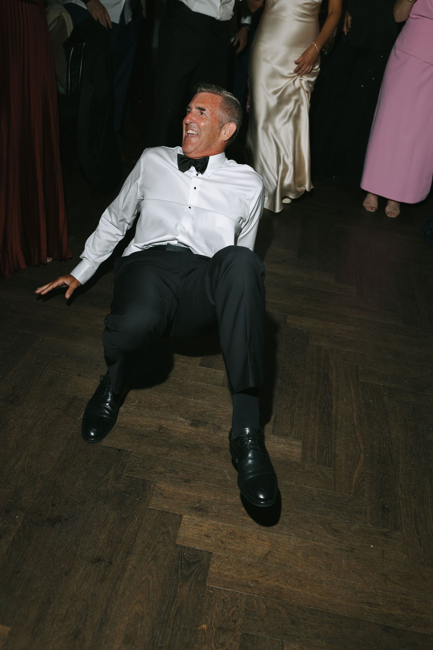 Person in formal attire sitting on wooden parquet floor during wedding reception.