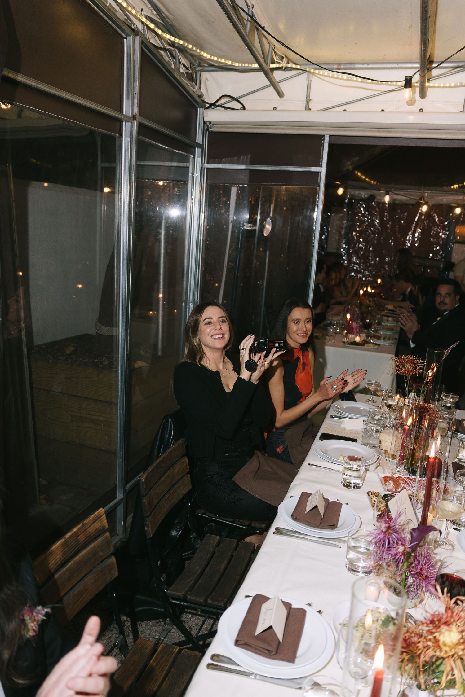 Guests seated at an elegant dinner table with place settings and string lights creating a festive atmosphere.