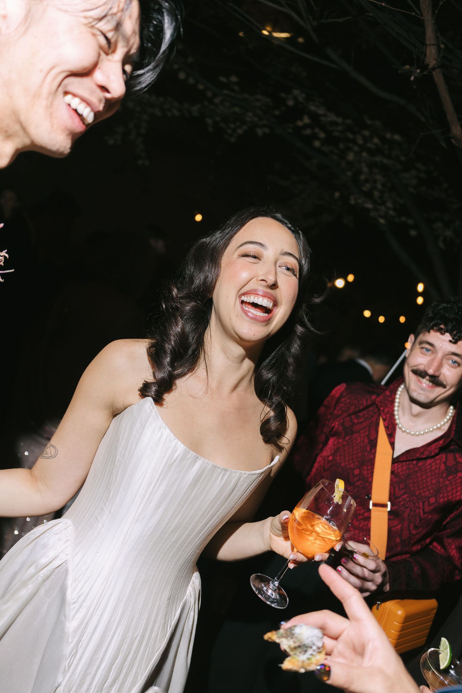 A joyful moment captured at a wedding celebration with guests laughing and holding drinks.