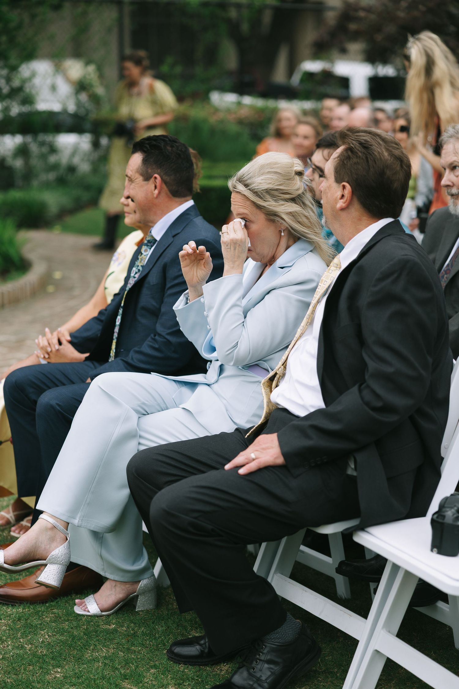 Wedding guests seated in white folding chairs on grass during outdoor ceremony.