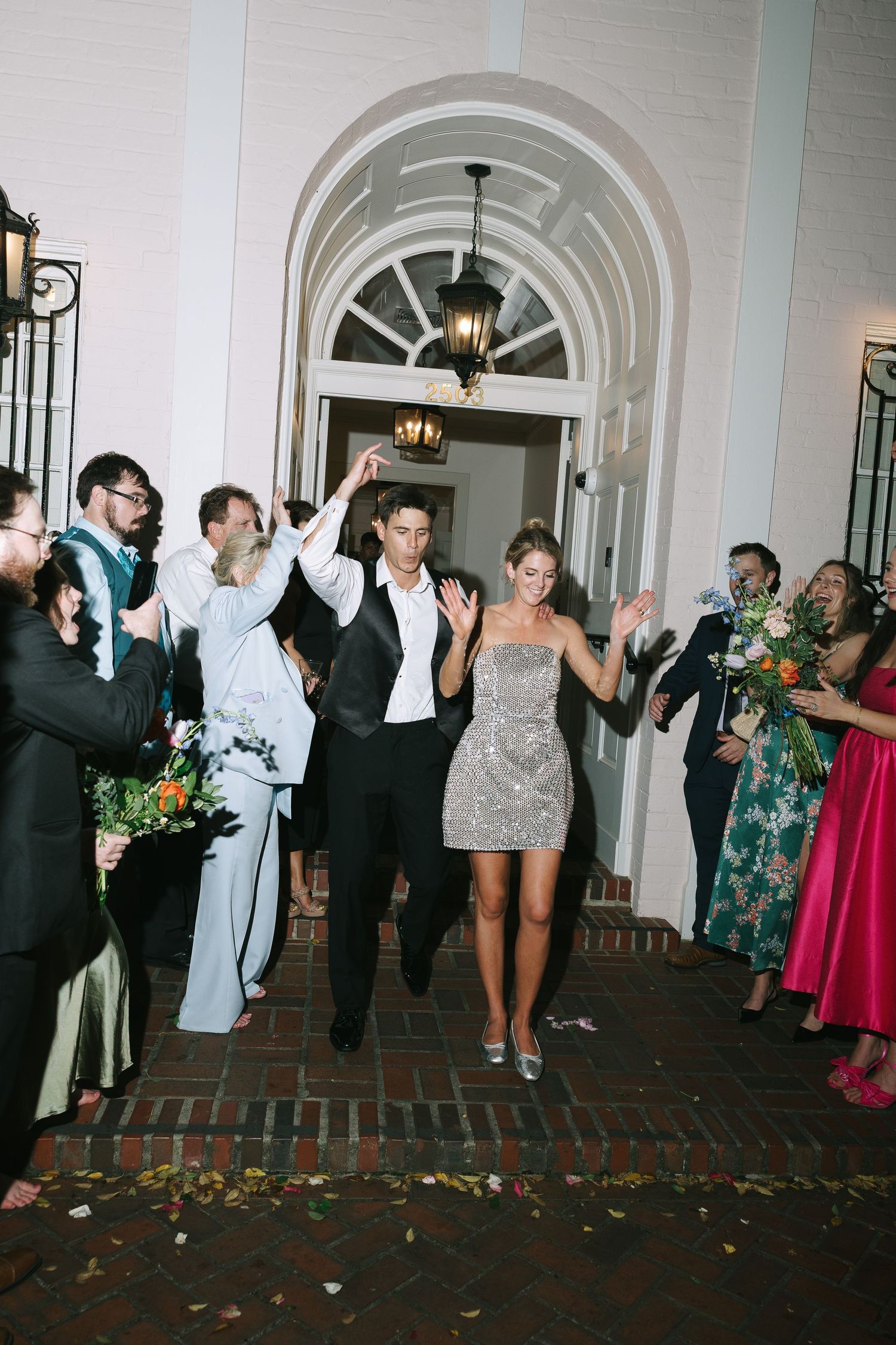 Wedding guests line an arched hallway celebrating as the couple makes their exit.