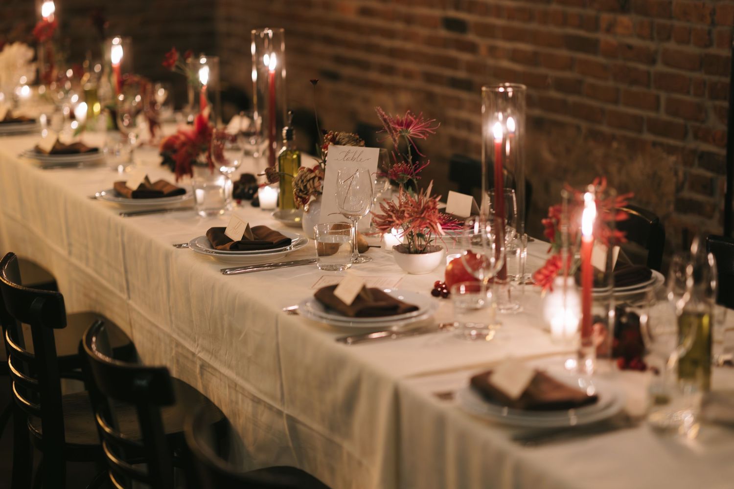 Elegant wedding reception tables set with candles and white linens against exposed brick walls.