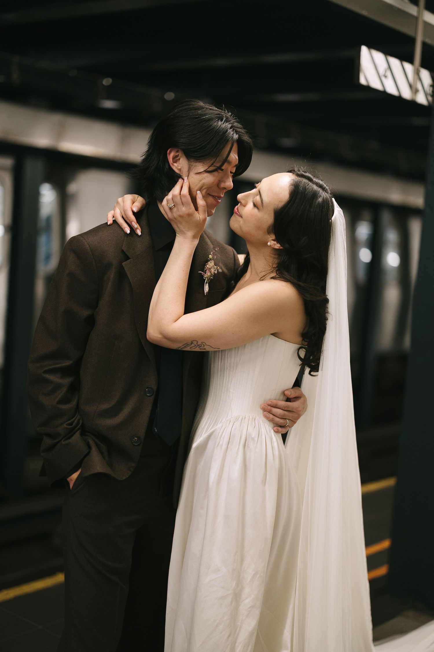 Bride in flowing white dress embraces groom in dark suit during intimate moment.