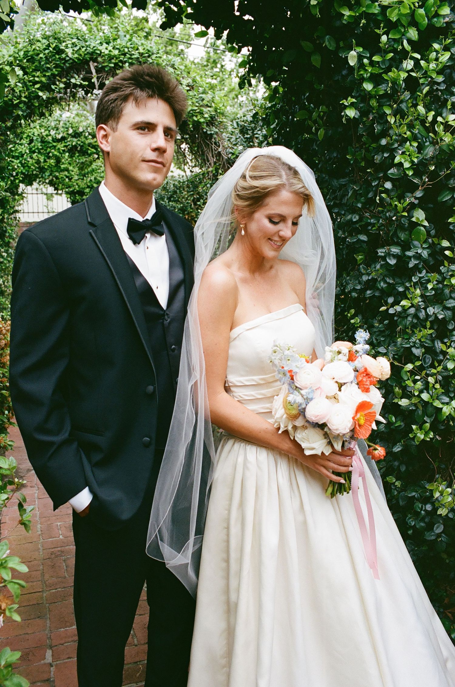 A couple shares an intimate moment in front of lush greenery during their wedding.
