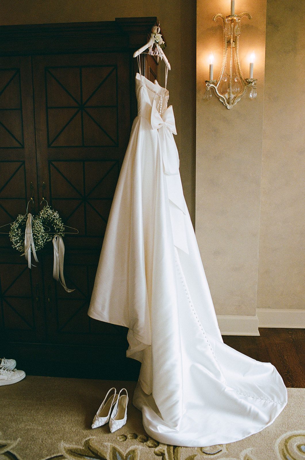 An elegant white wedding gown hangs on display with matching shoes beneath.