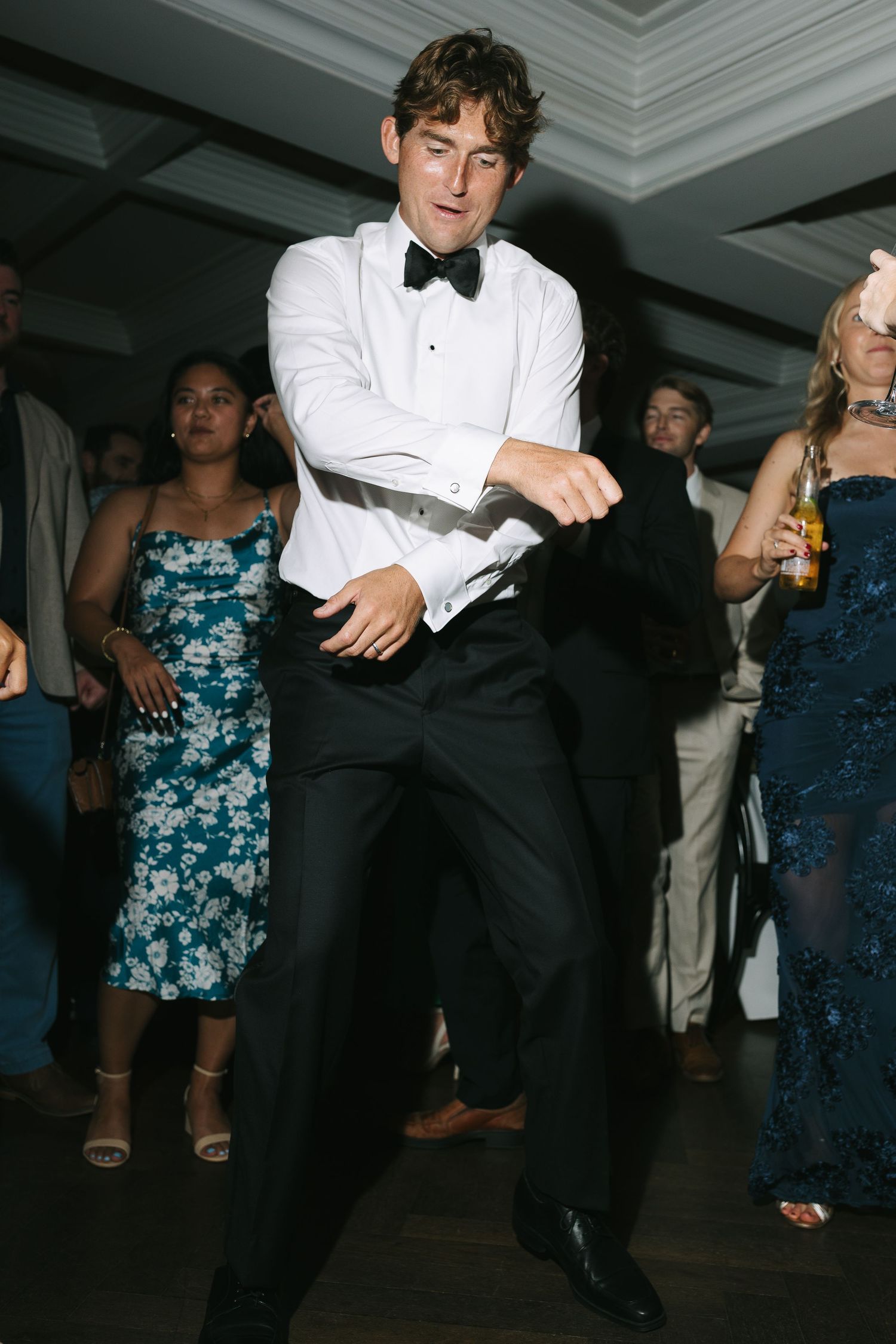 Guests dancing energetically at an indoor wedding reception with elegant decor and lighting.