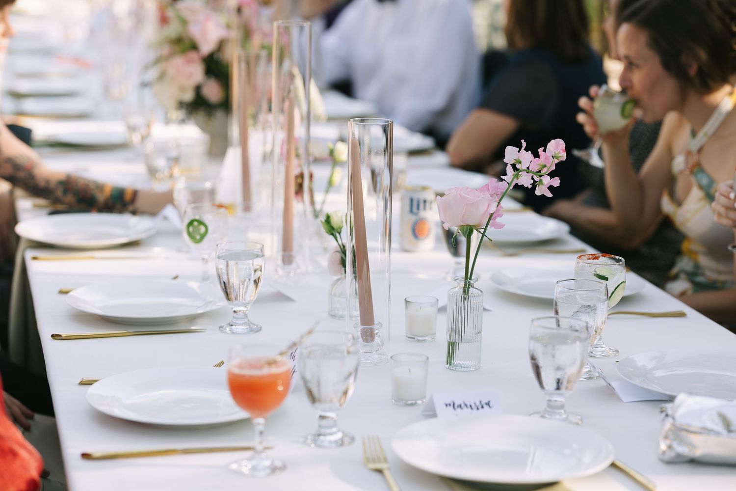 Close-up of formal place settings with glassware and pink cocktails on white tablecloths.