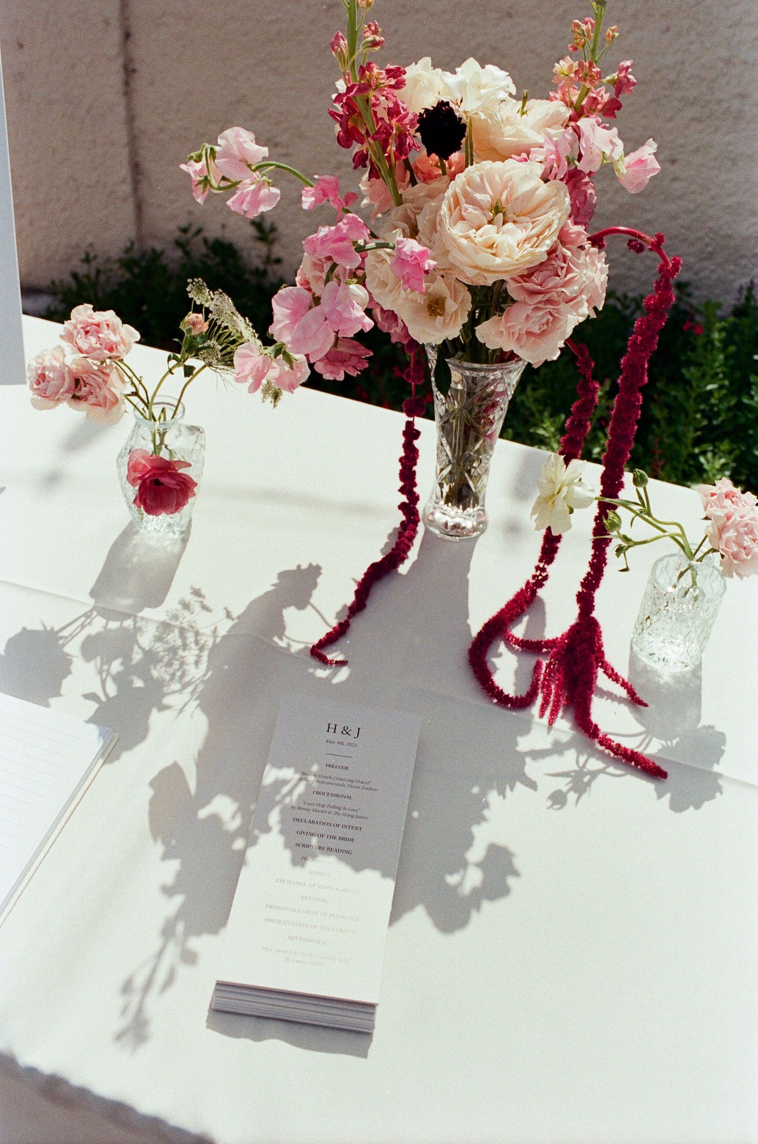 Pink and white floral centerpieces with burgundy accents on a white tablecloth.