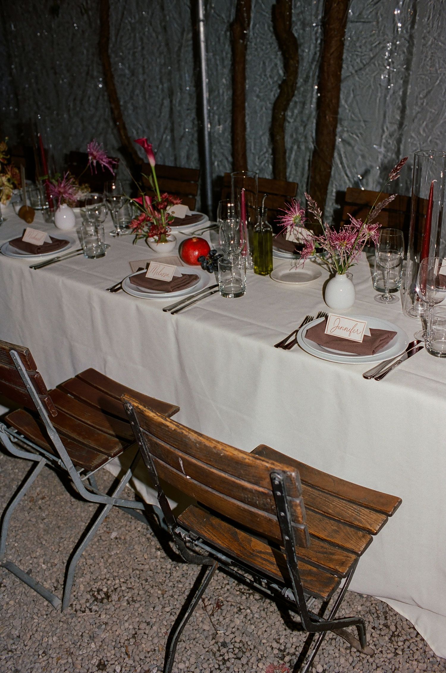 Elegant table setting at an outdoor dining event with wooden bench seating and white linens.