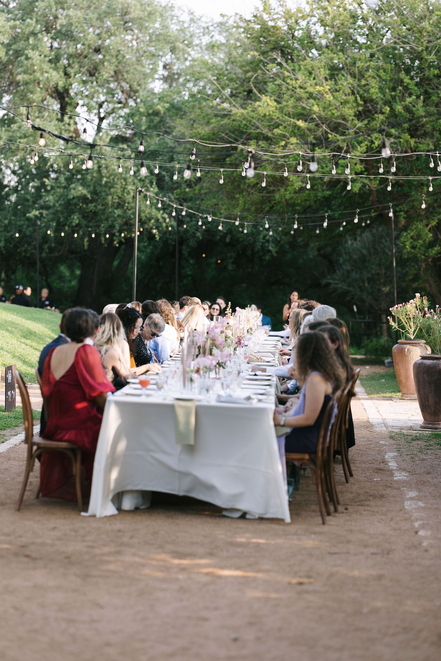 Outdoor wedding reception area with string lights and long dining tables under trees.