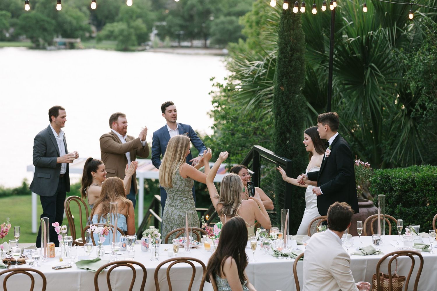 Outdoor wedding reception setup with string lights and wooden chairs.