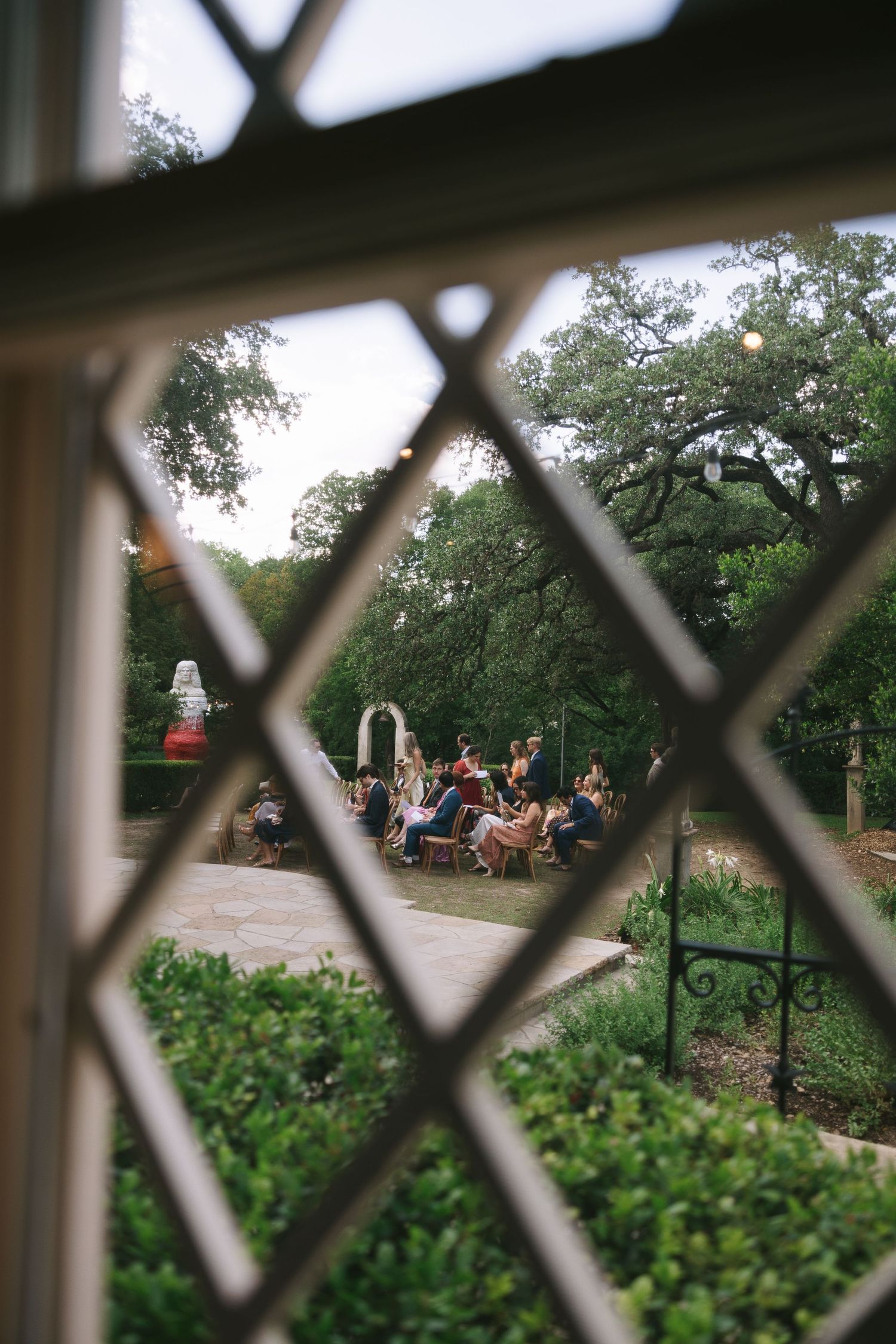 View through latticed window of an outdoor garden ceremony setup with chairs and greenery.