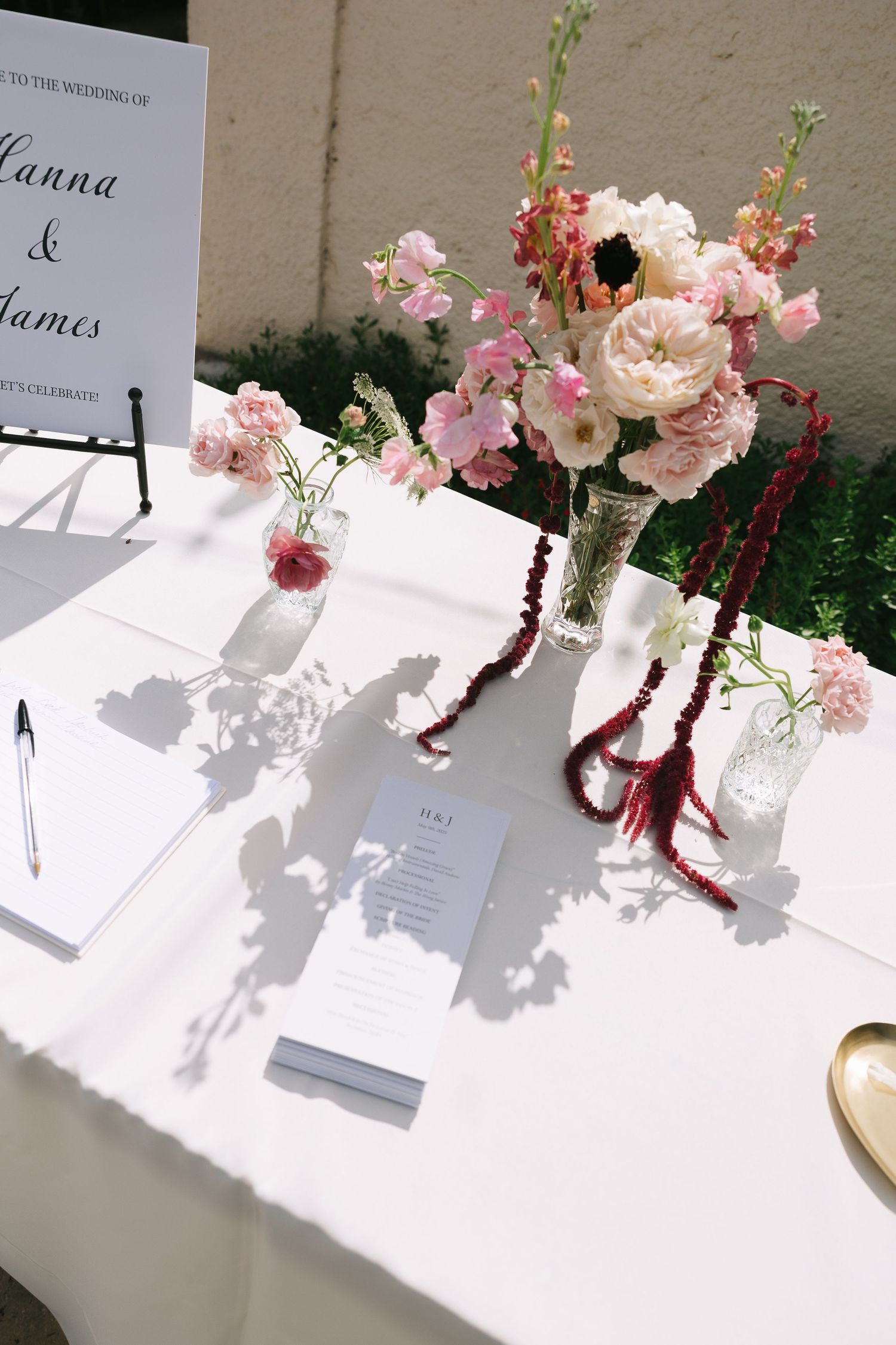Wedding invitation and floral centerpieces on white tablecloth with dramatic shadows.