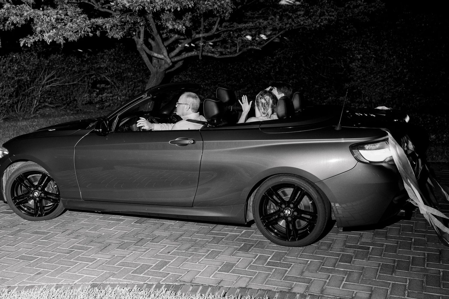 A black and white image of people in a convertible car during an evening celebration.