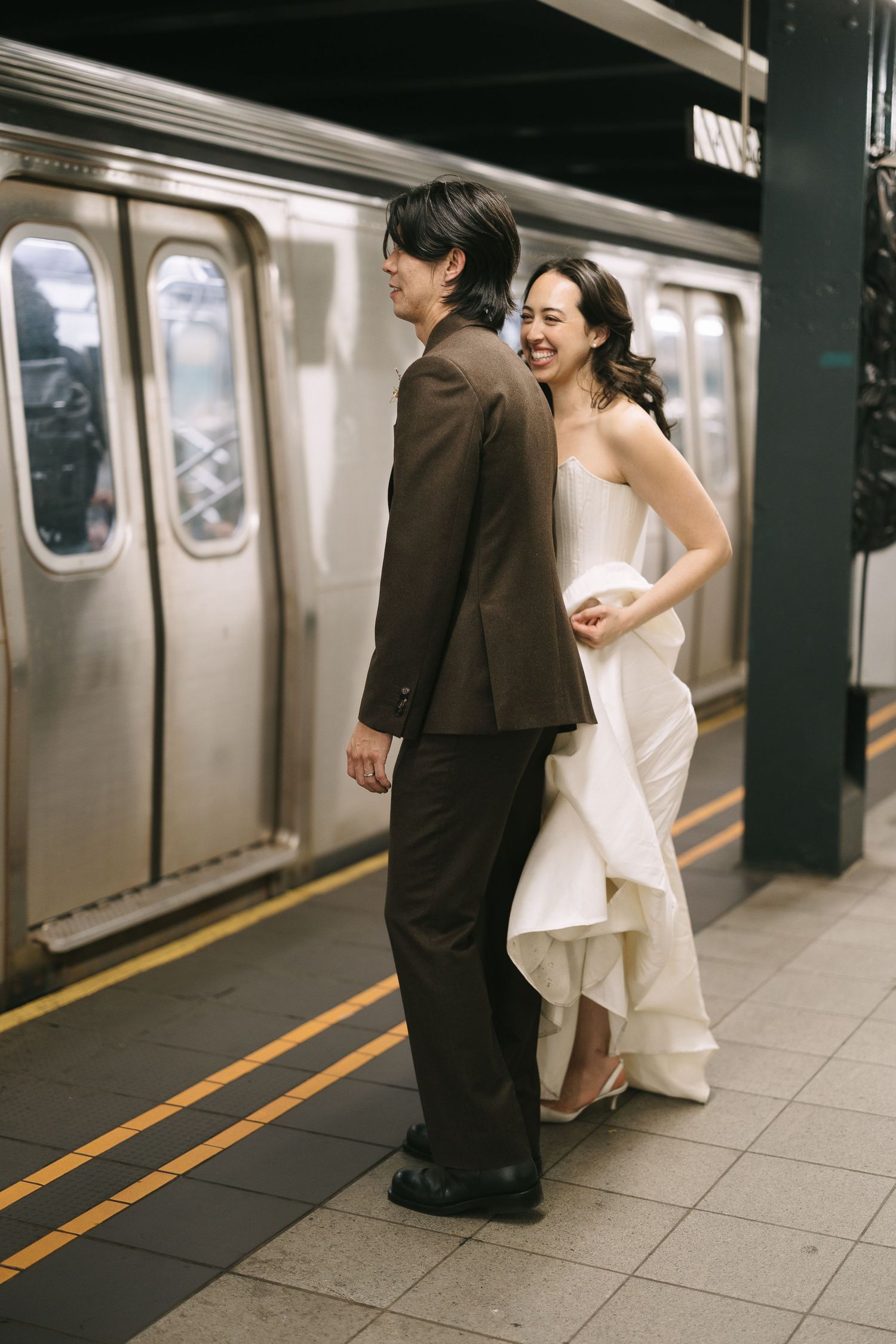 Bride and groom share romantic moment on subway platform with train in background.